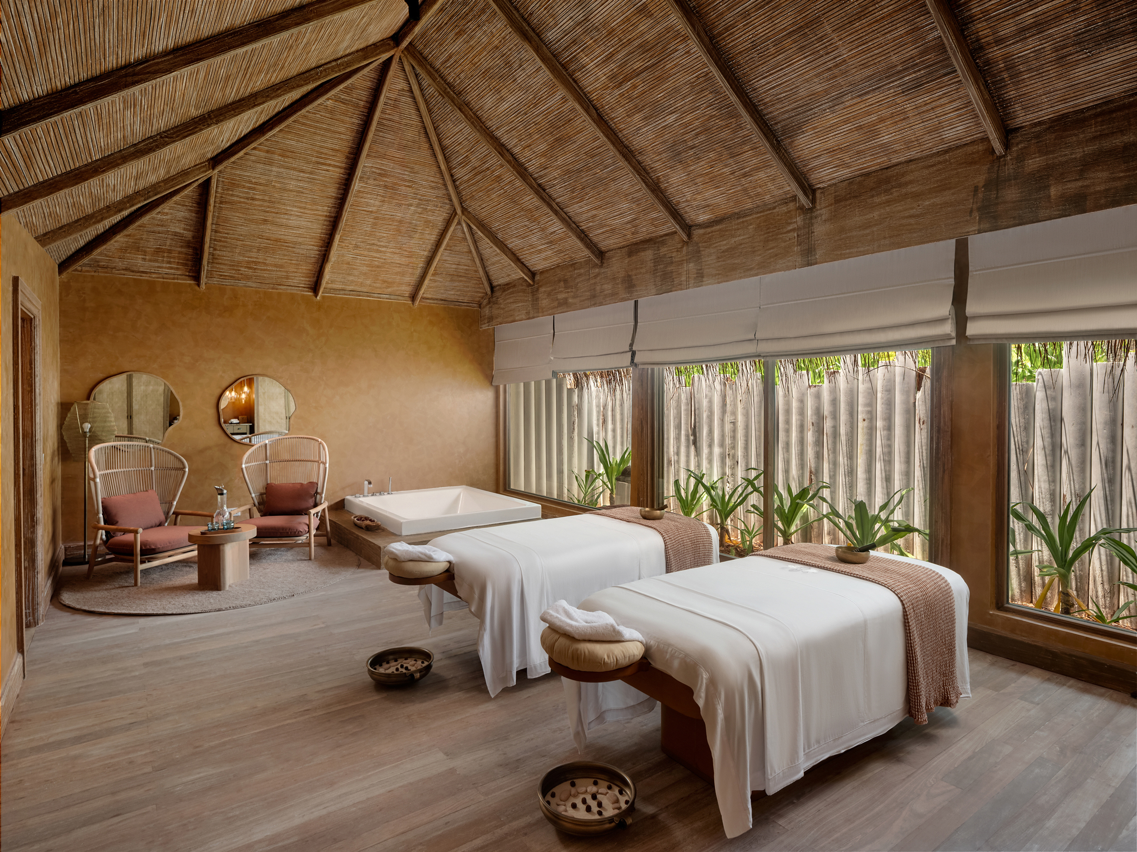 Couples treatment room with two massage beds and rattan chairs in the spa at Six Senses Kanuhura