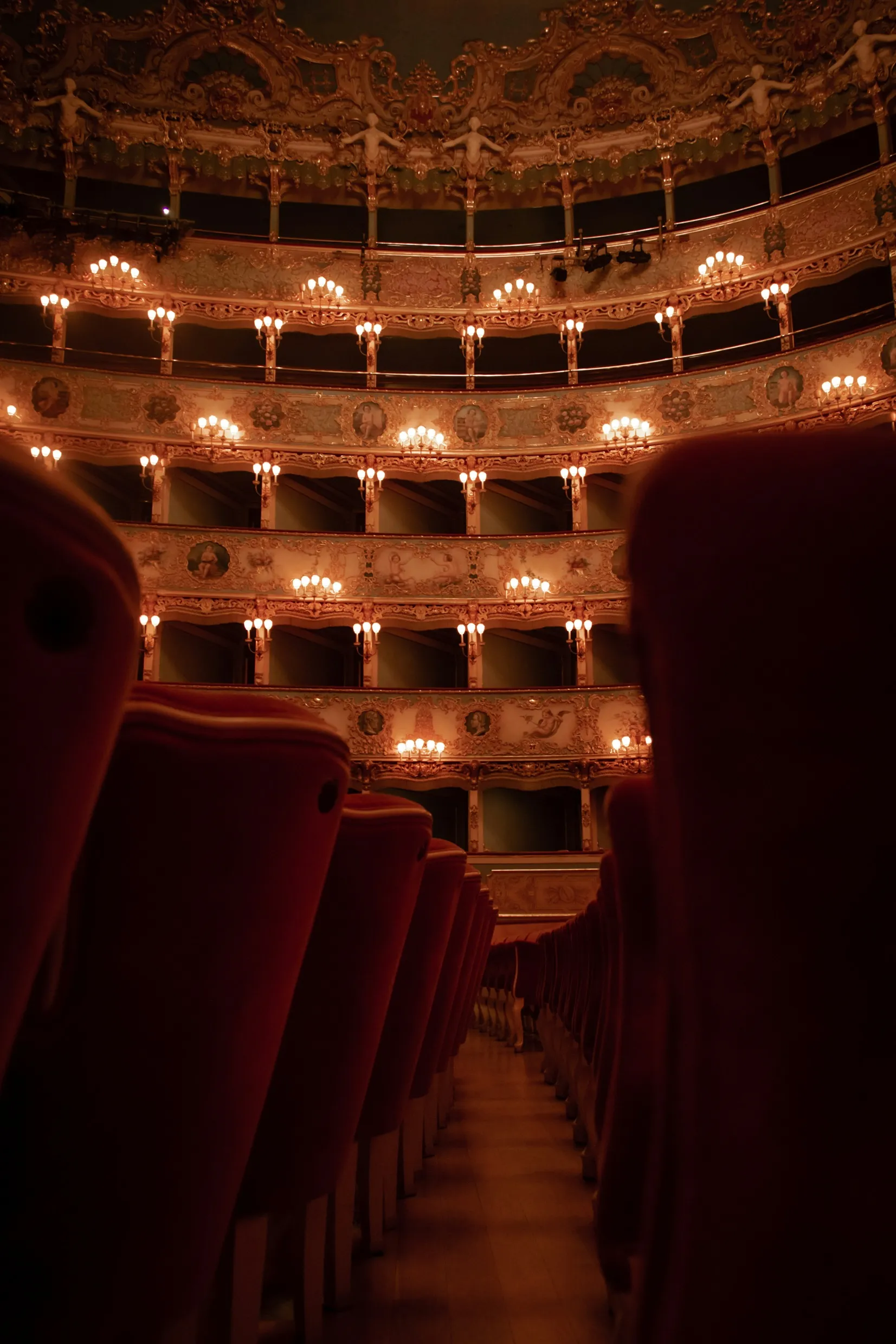 Ornate theater interior with balconies, chandeliers, and intricate decorations viewed from audience seating
