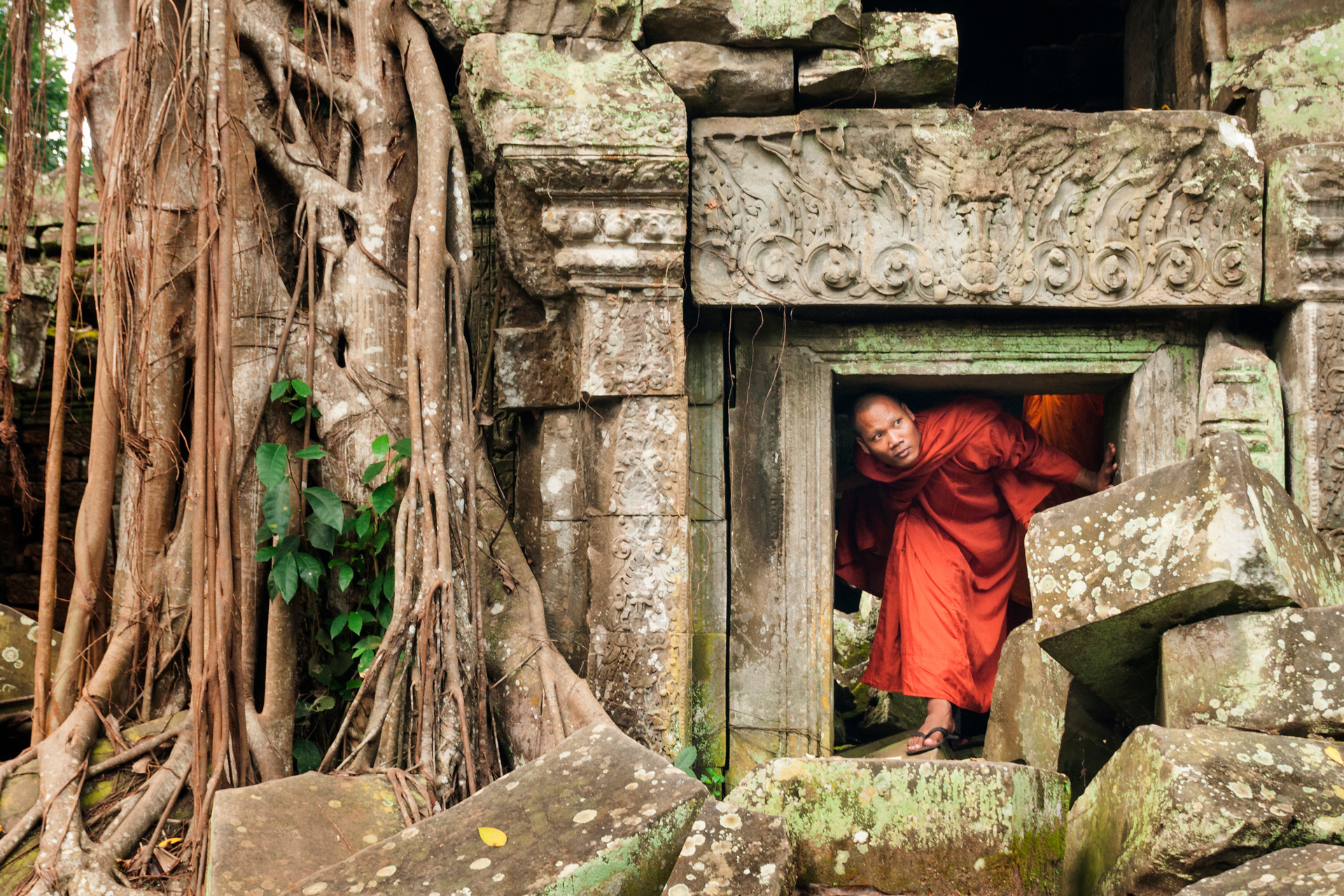A monk in orange robes looking from a small gap in an old temple