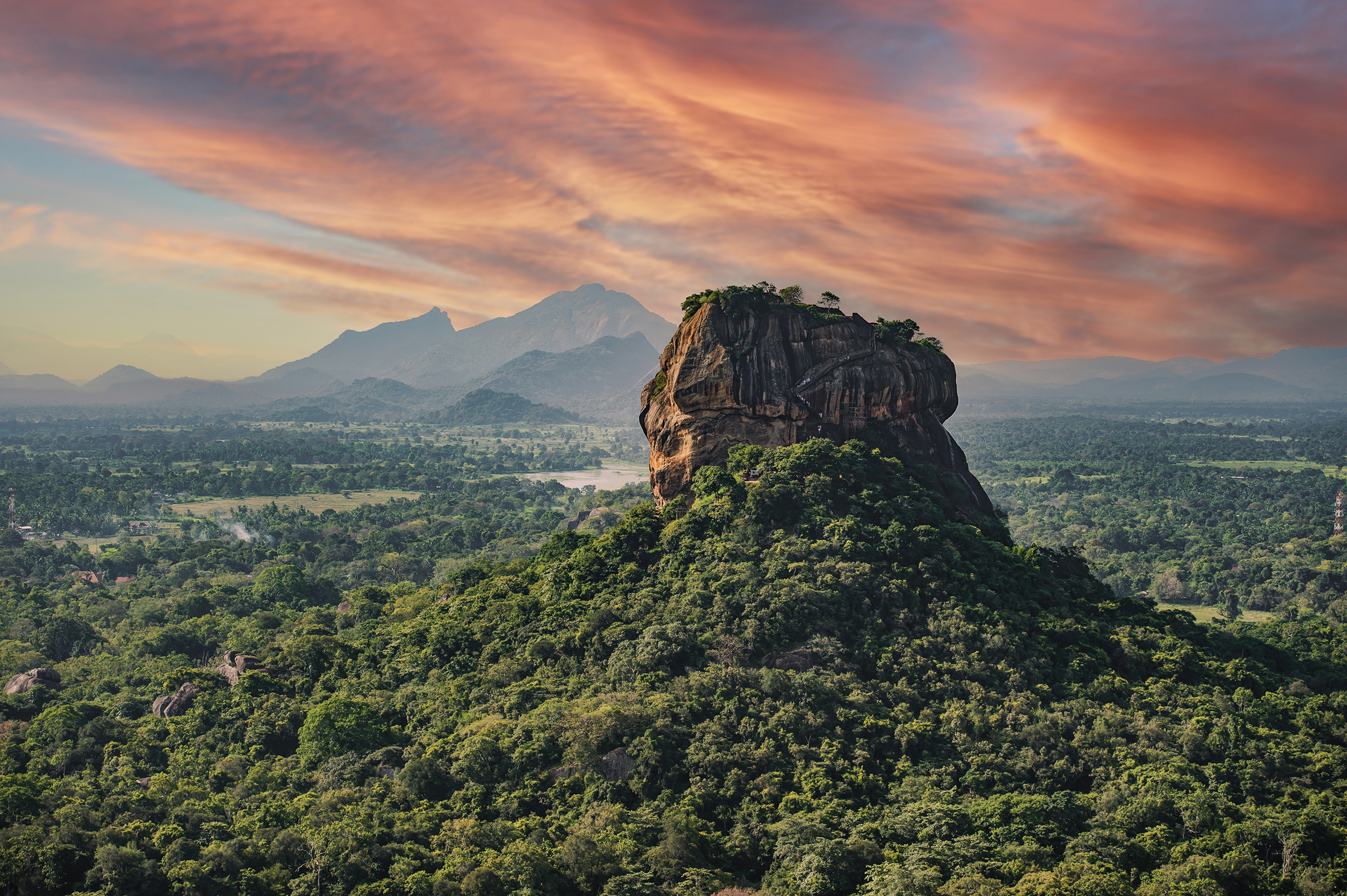 Sigiriya rock fort in Sri Lanka towering above a green landscape set against a pink sky
