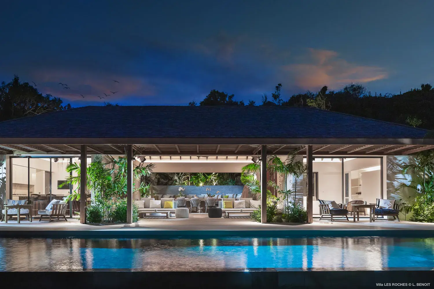 Nighttime view of Les Roches Villa in St Barths showcasing the open‑air living pavilion, elegant lighting and serene poolside ambiance.