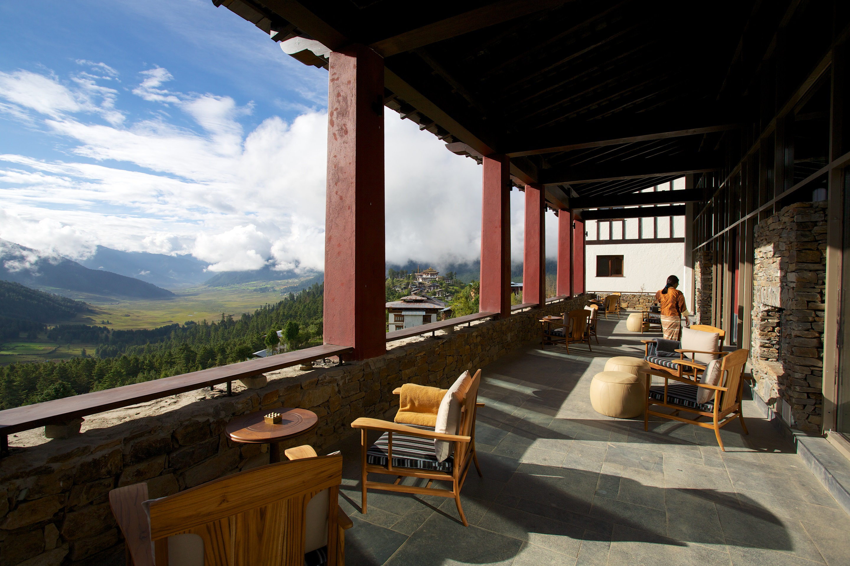 Terrace with outdoor cushioned chairs and small tables overlooking a green valley.