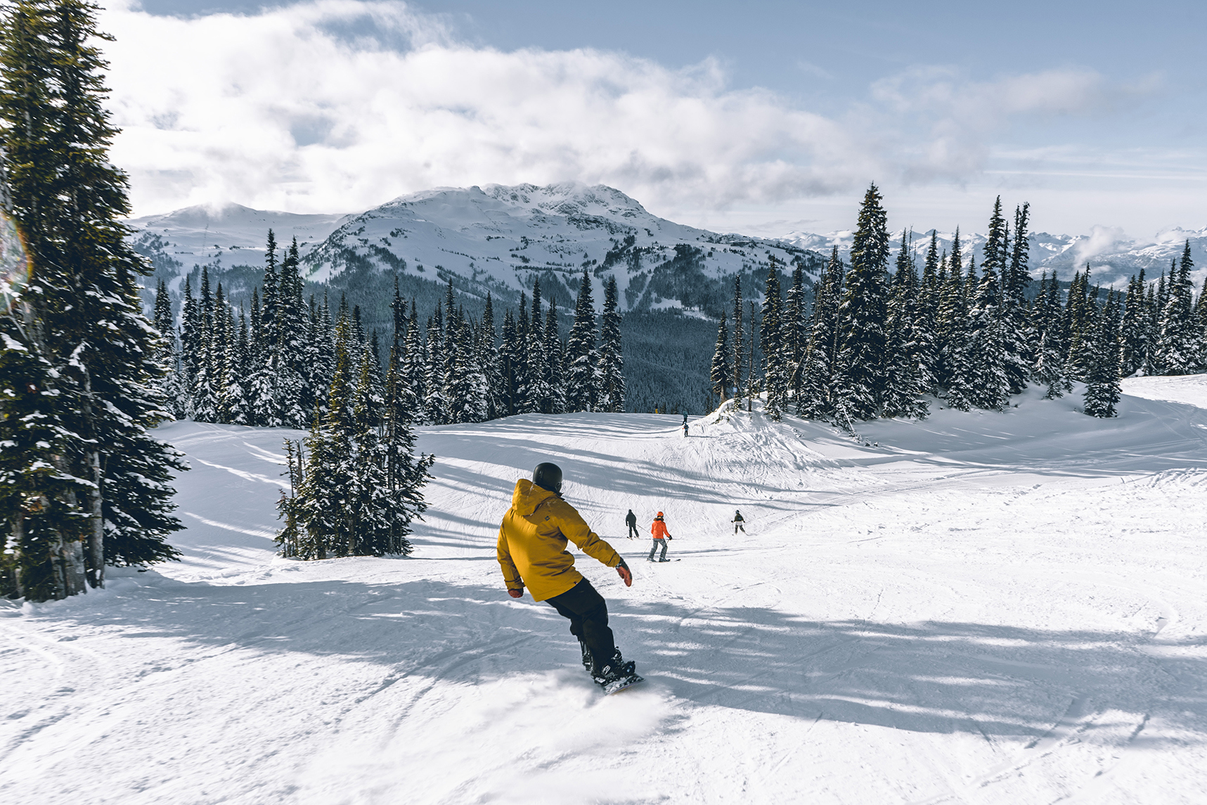 Snowboarder in yellow jacket following others down a snowy hill
