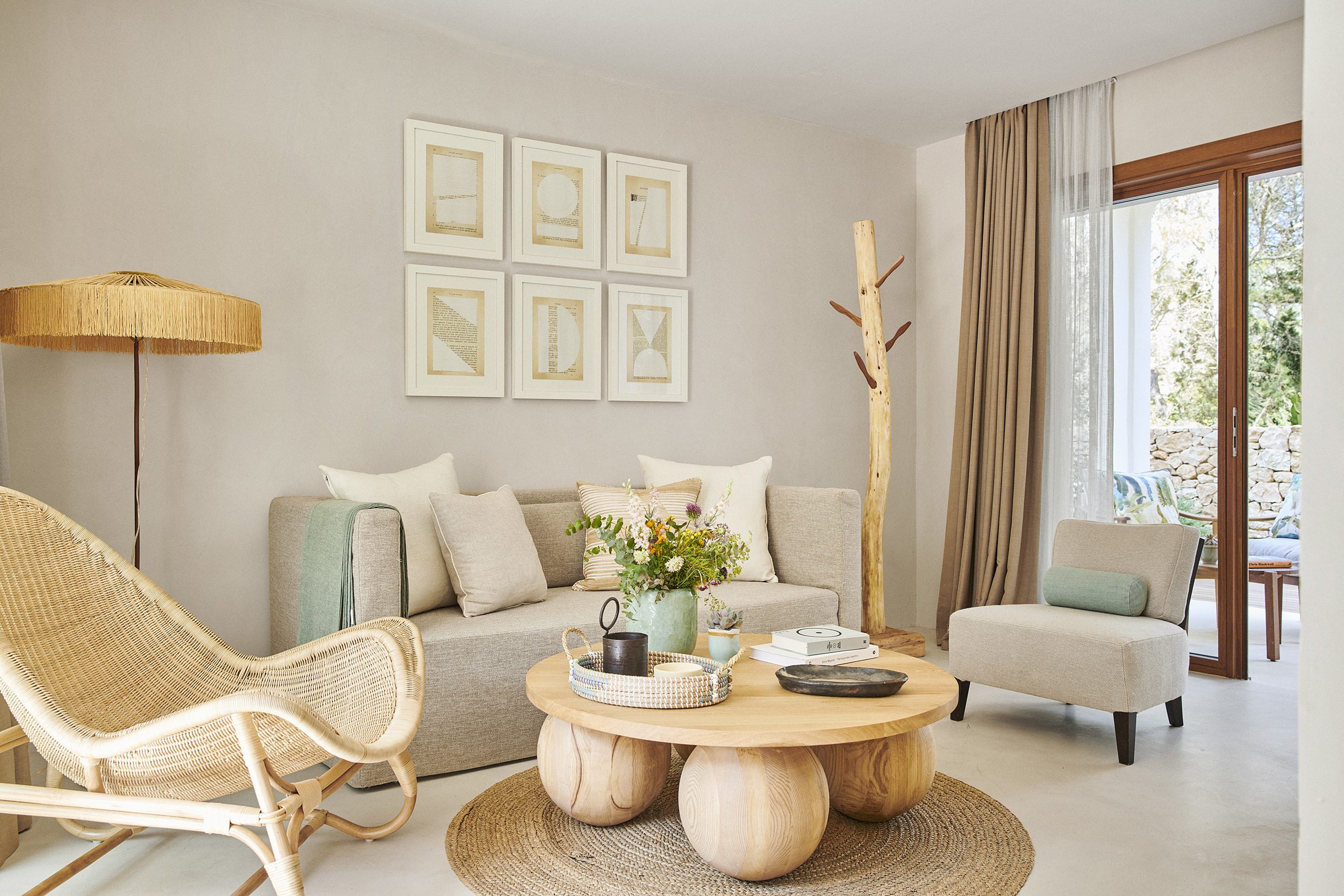 The lounge of a one bedroom suite at Teranka featuring bohemian woven furniture decorated with neutral soft furnishings, a coffee table set with books and a vase and artwork on the walls, with a glimpse of a terrace through glass doors