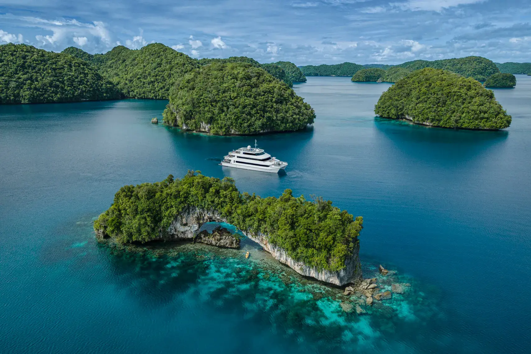 An aerial view of Four Seasons Explorer Palau anchored between the lush and jungly island of Palau beneath a clear sky