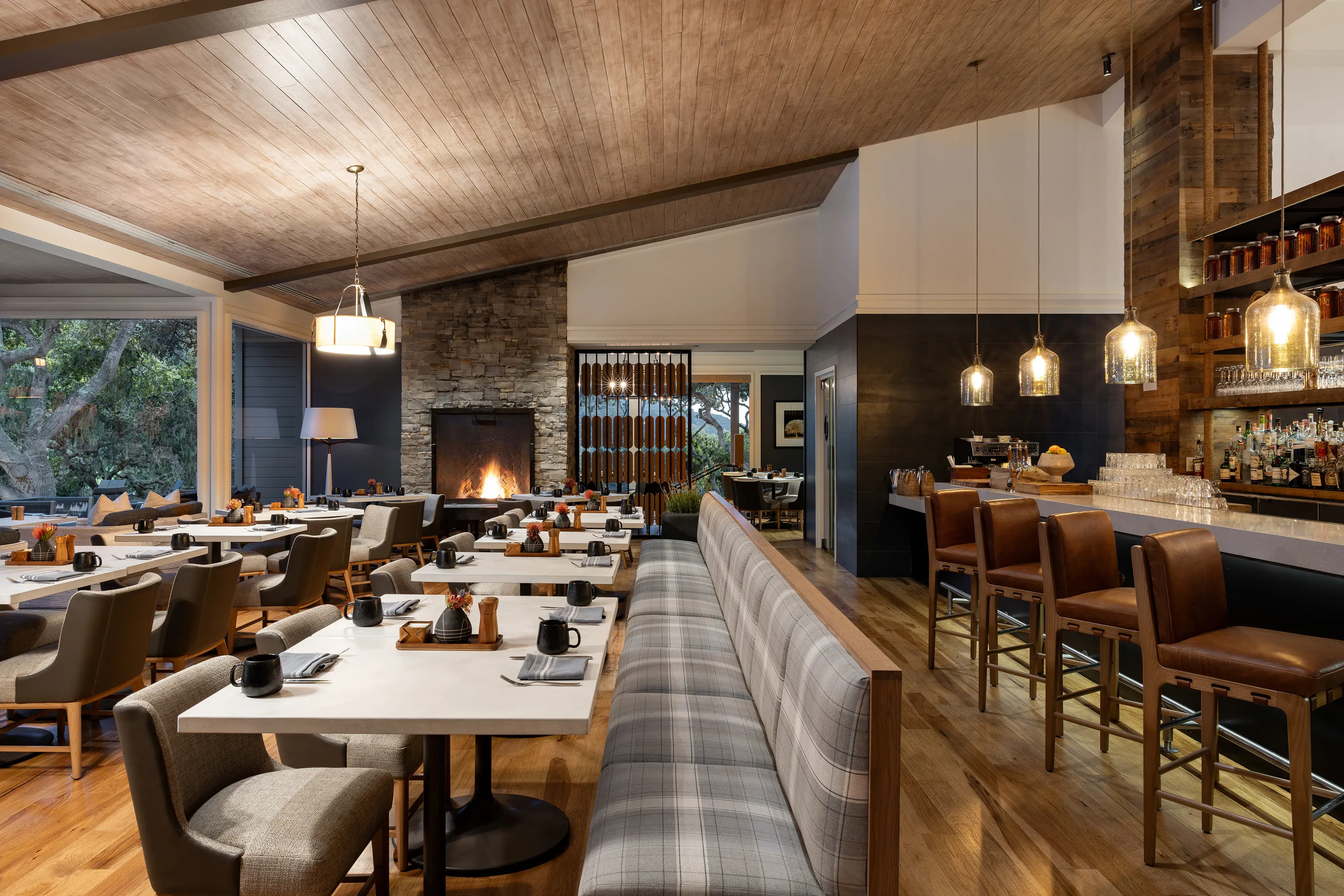 The modern Kitchen Restaurant at Carmel Valley Ranch in California featuring tables set for dinner along a large bench and a bar with stools behind
