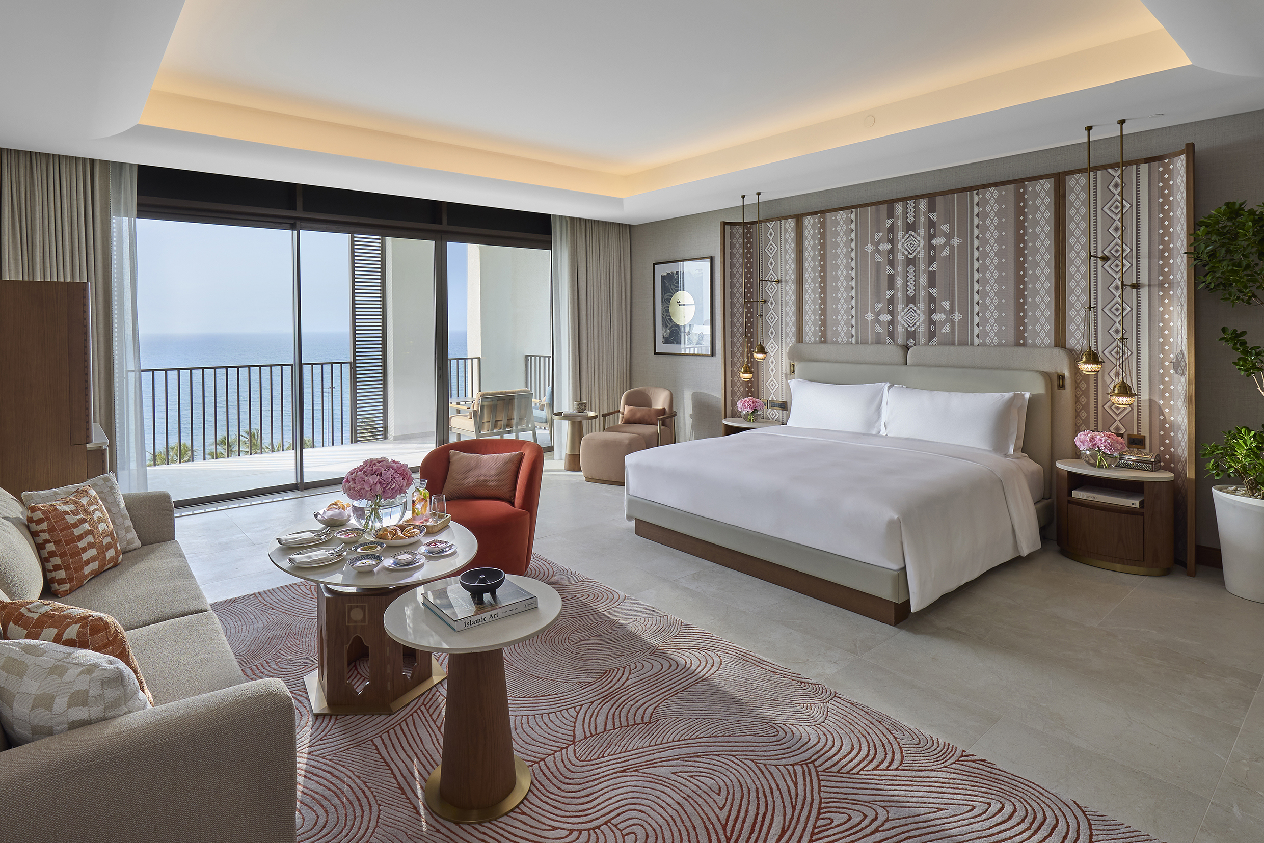 A large suite bedroom at Mandarin Oriental Muscat featuring a large bed, plush seating area and soft furnishings in traditional patterns