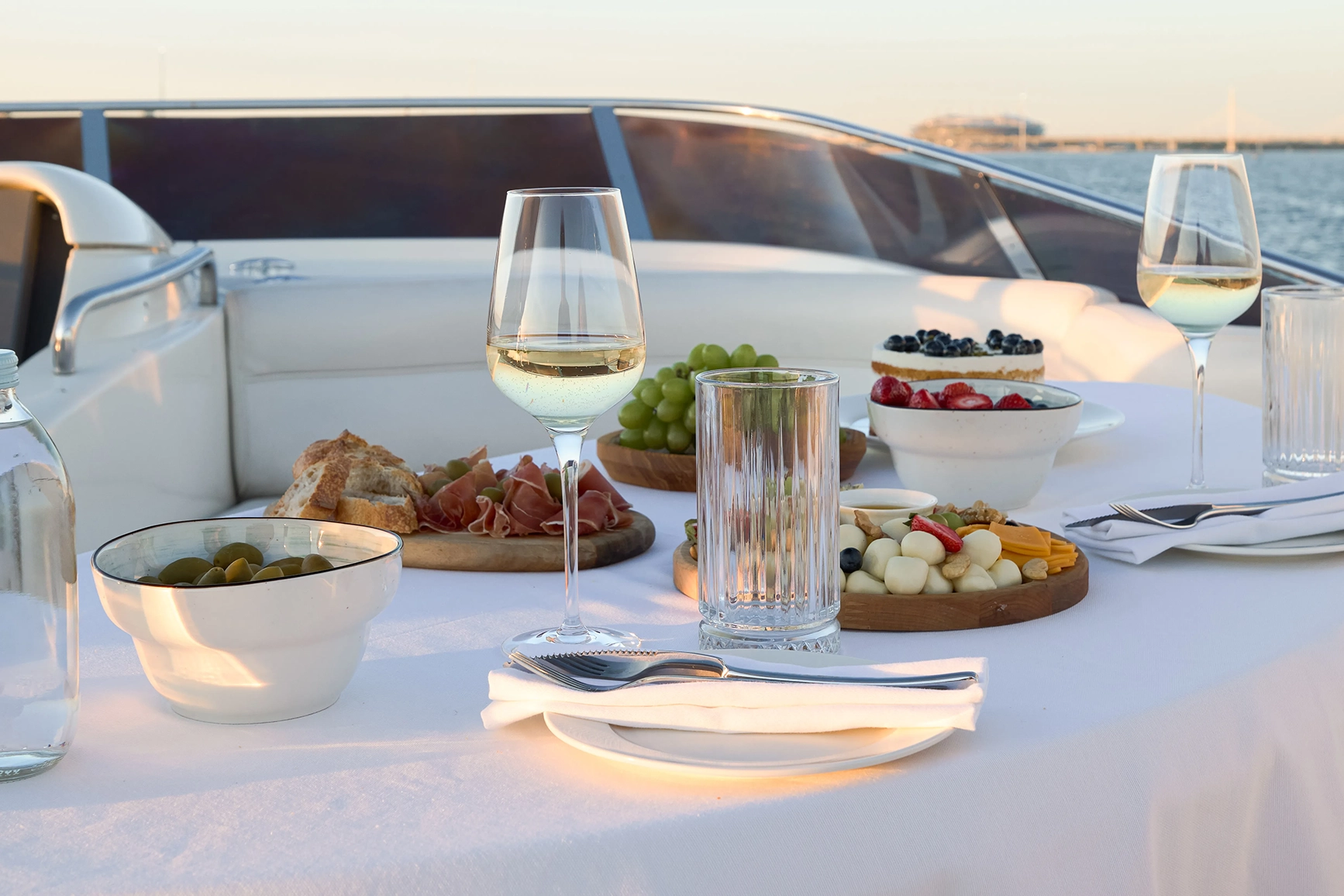 A table on a private yacht with wine glasses, nibbles, fruit and charcuterie