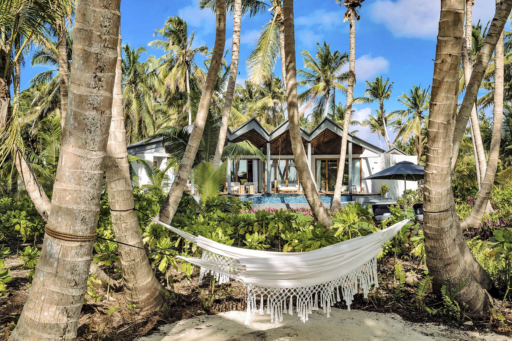 Two white hammock strung between palm trees in the gardens of a pool villa