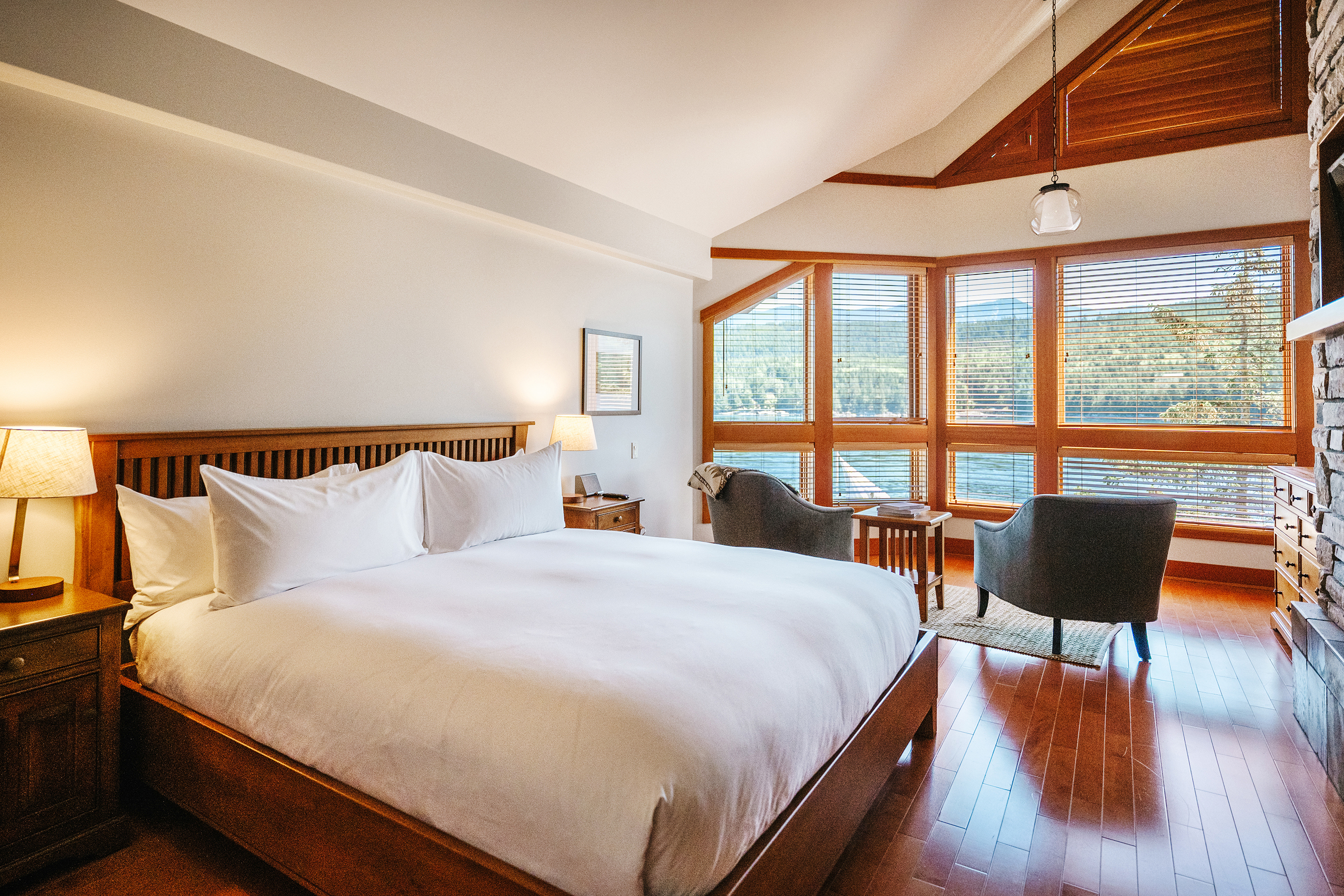 A master bedroom in Yuculta Lodge with a bed featuring white linens and two chairs facing the view 