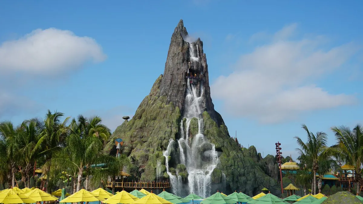 Tropical waterpark scene featuring a towering volcano with cascading waterfalls under a bright blue sky at Universal Volcano Bay in Orlando.