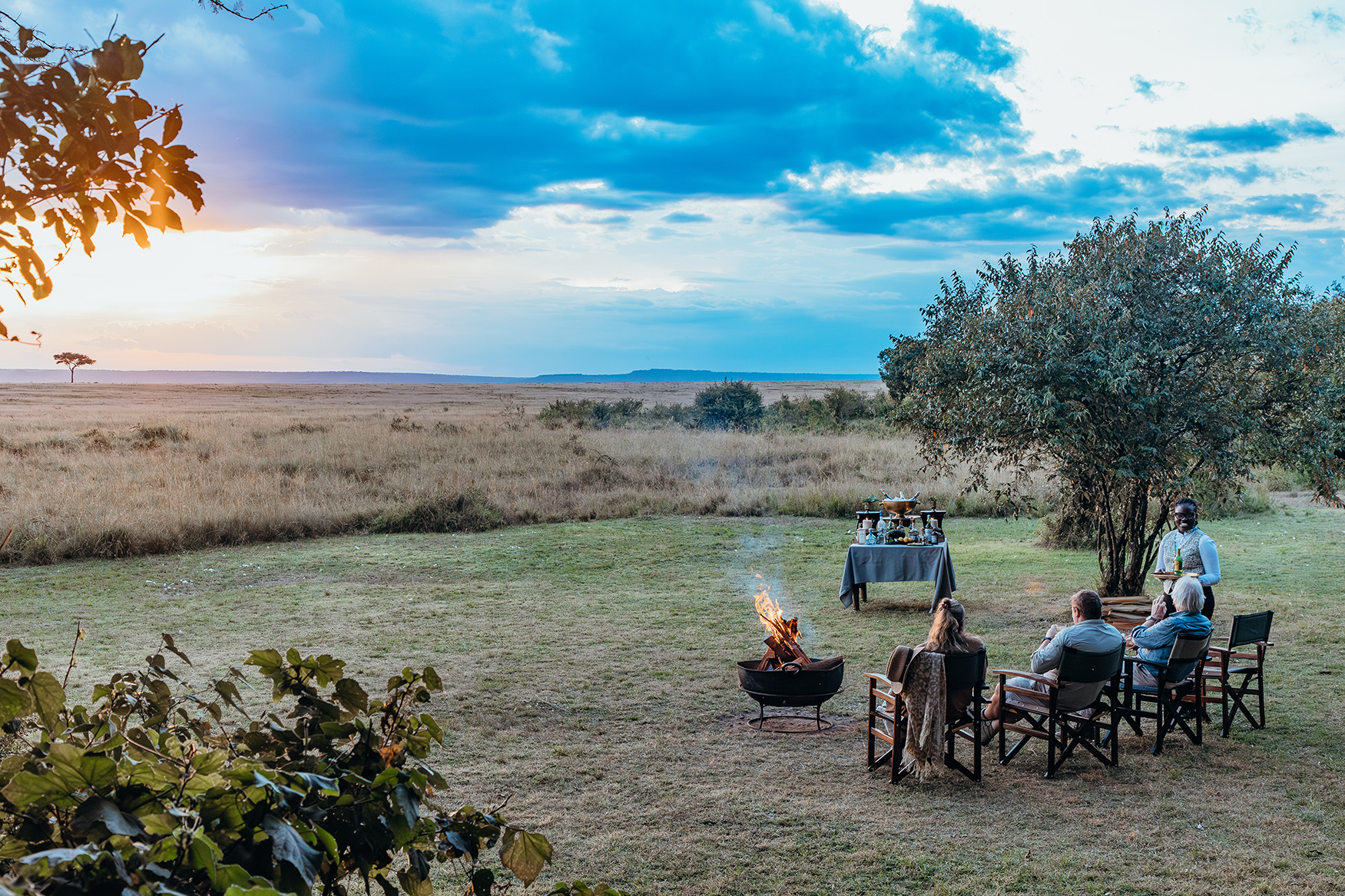 Africa, Kenya, Mara Plains Camp, group enjoying a sundowner by a firepit 