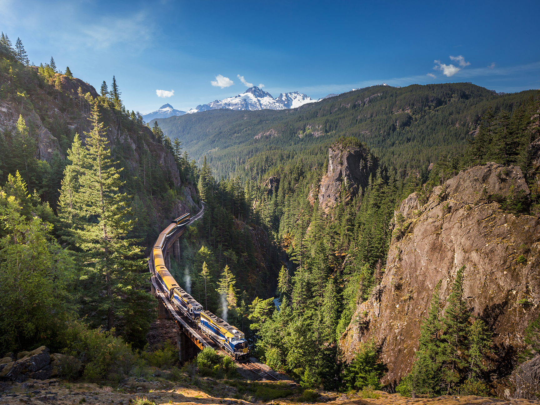 Rocky Mountaineer train on tracks going through mountain forests