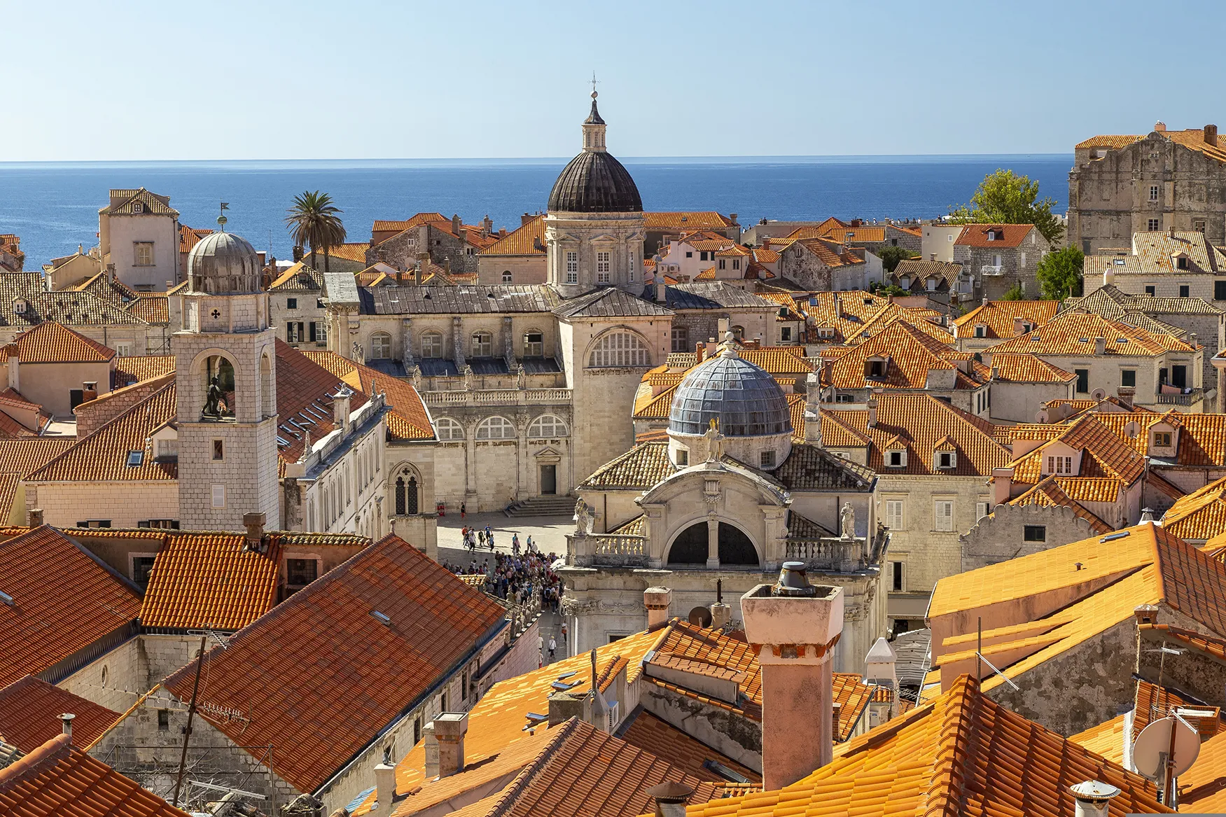 Elevated view of Dubrovnik’s old town with terracotta rooftops, historic church domes, and the Adriatic Sea in the background.