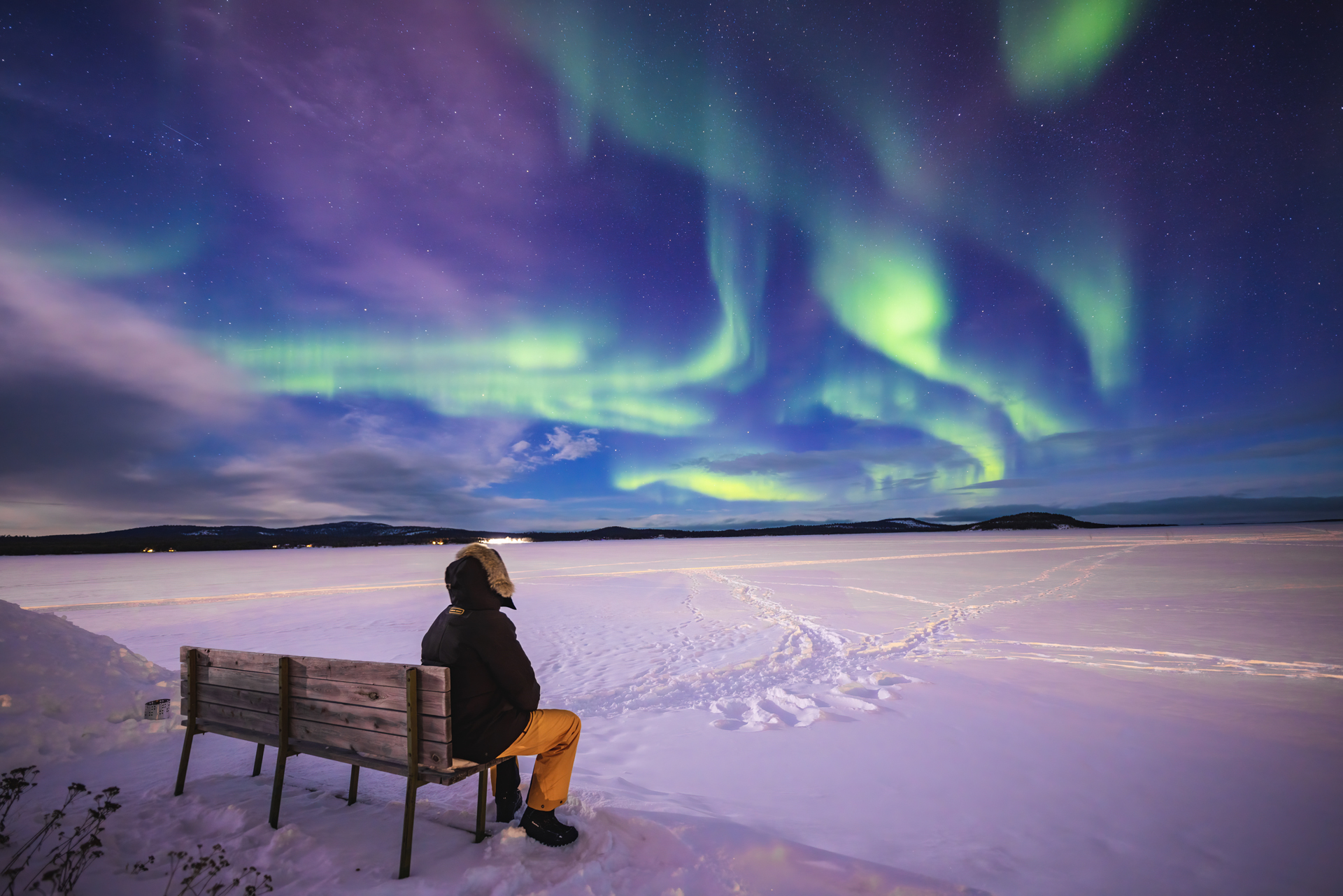 A person sat on a wooden bench looking up at the northern lights
