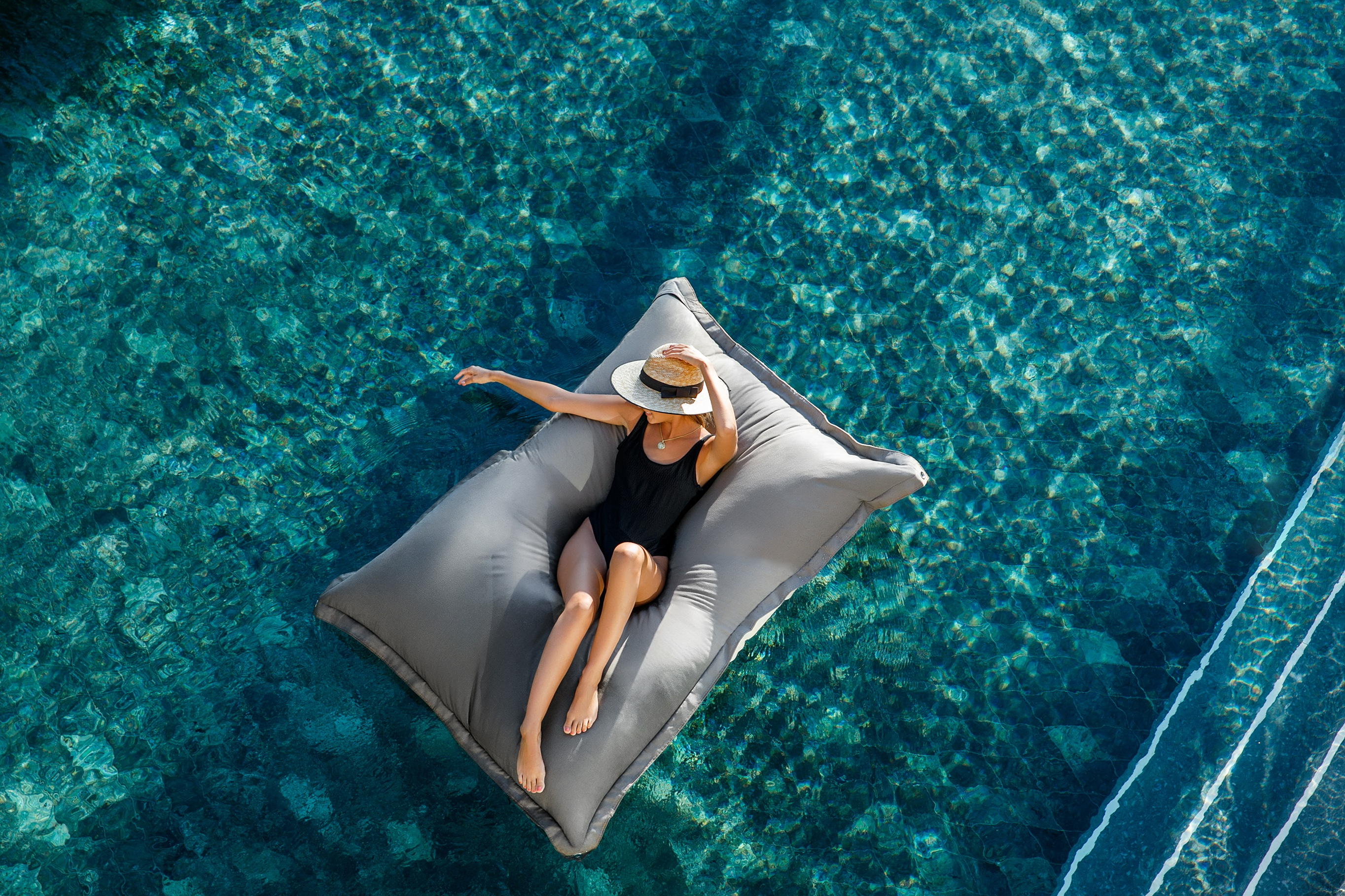 Guest relaxing on a floating daybed in a crystal-clear infinity pool