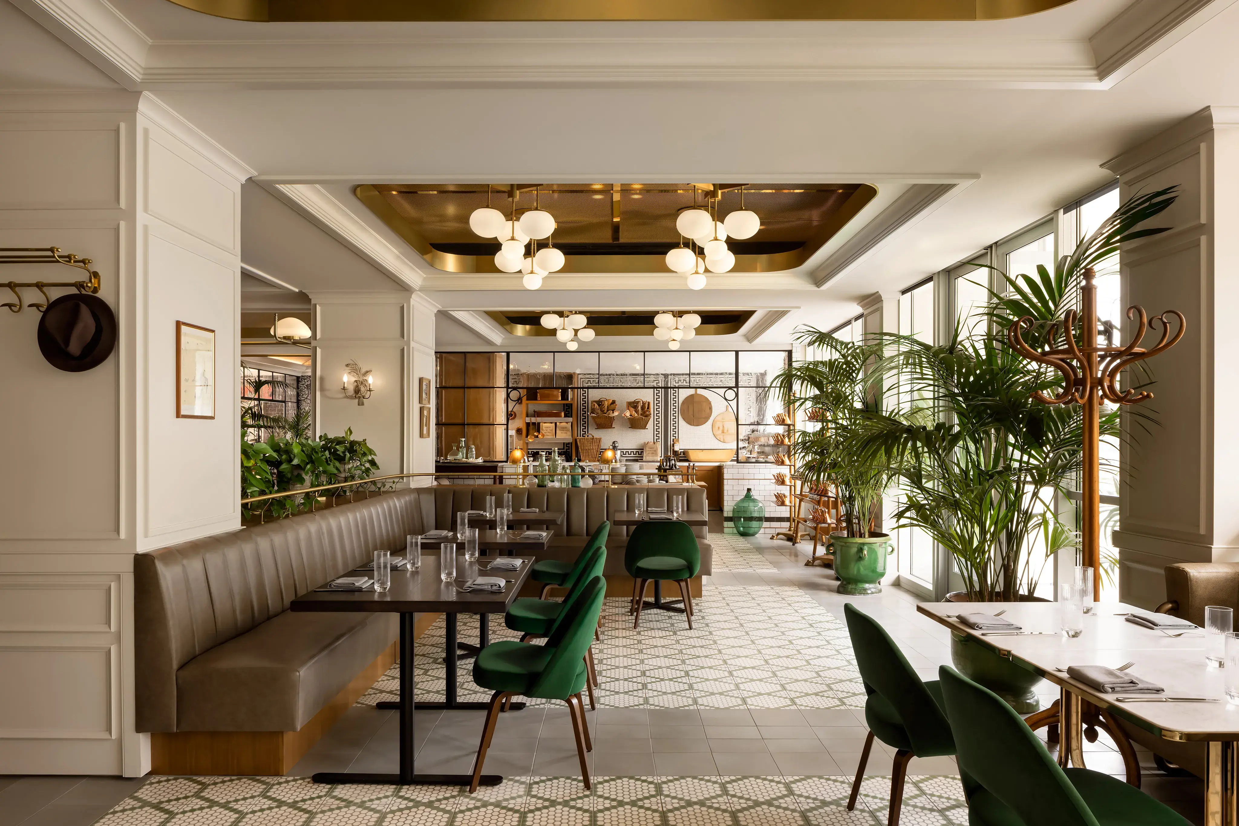 Chic dining room at Lumière in Fairmont Century Plaza Los Angeles featuring elegant banquette seating, gold accents, and lush indoor greenery.