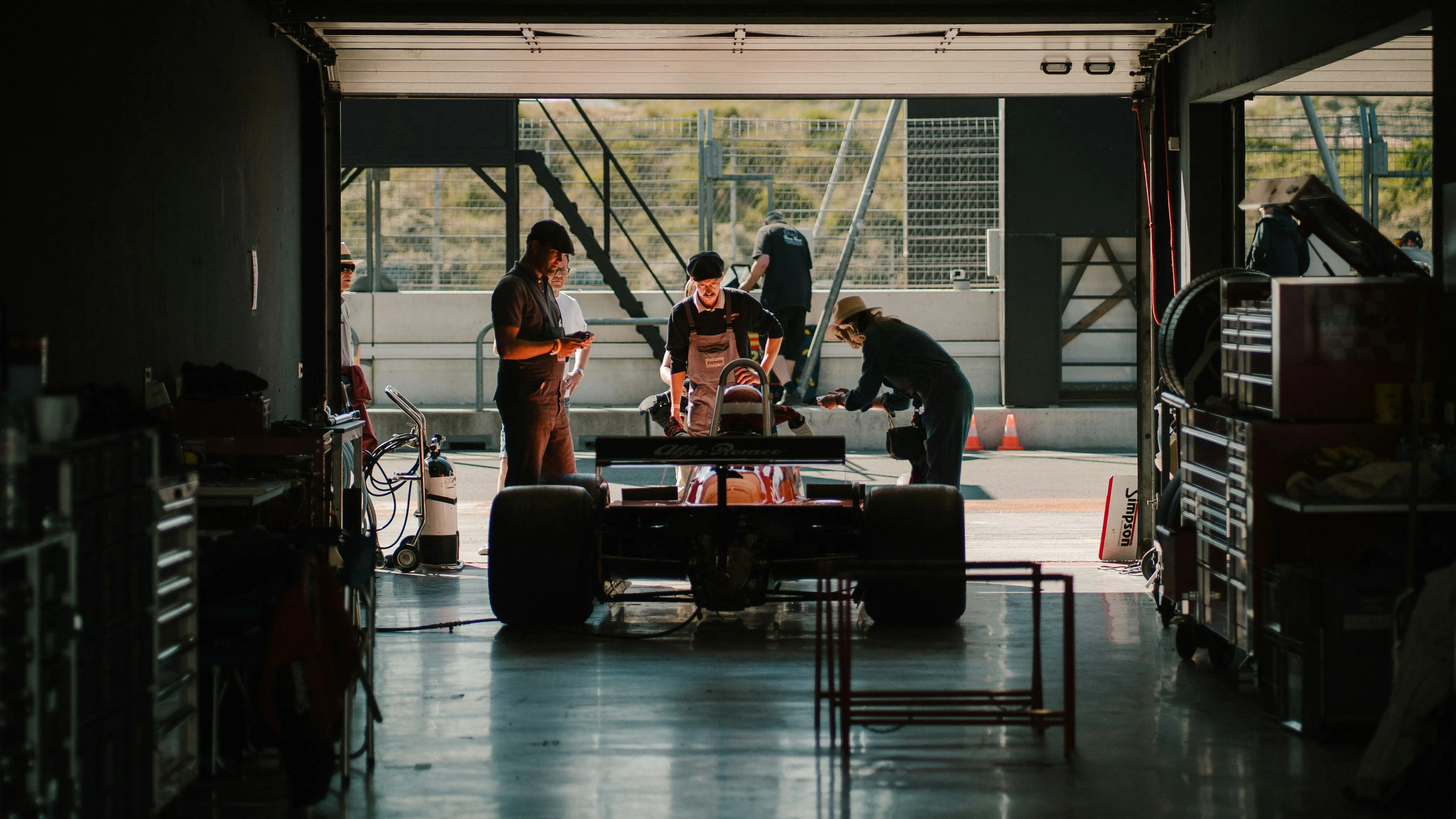 Formula race car inside a garage with mechanics performing maintenance and preparing for track session.