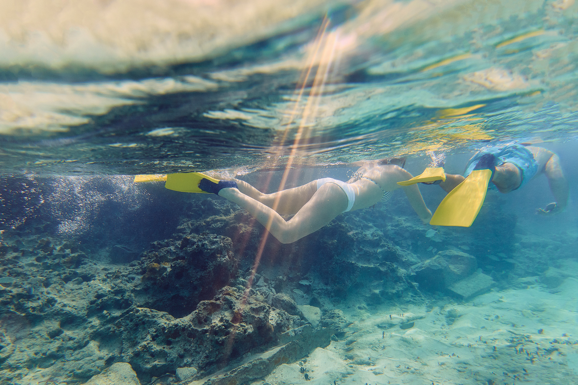 Two people snorkeling under water wearing orange flippers