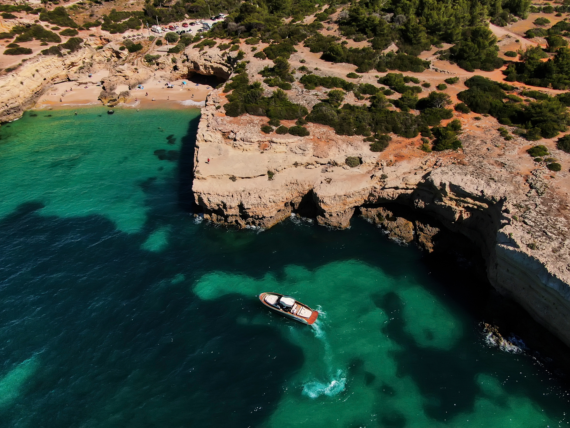 A rocky coastline with green trees and bushes with a boat on the sea