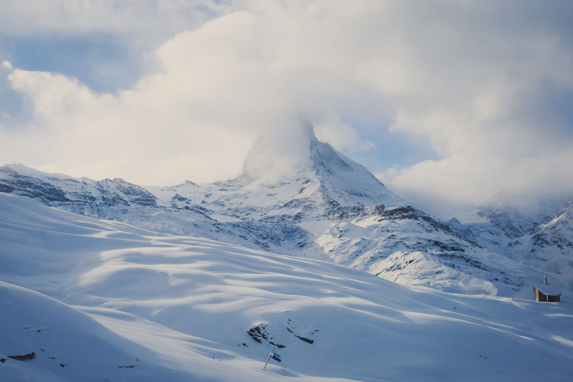 Snow hills leading up to the Matterhorn mountain that is partially covered by clouds