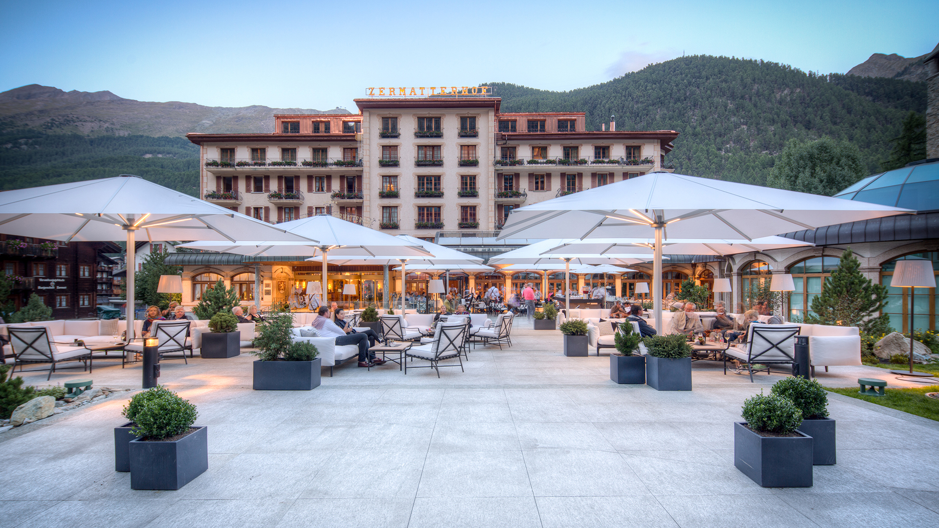 A grand patio featuring tables and umbrellas with a view of the hotel in the background