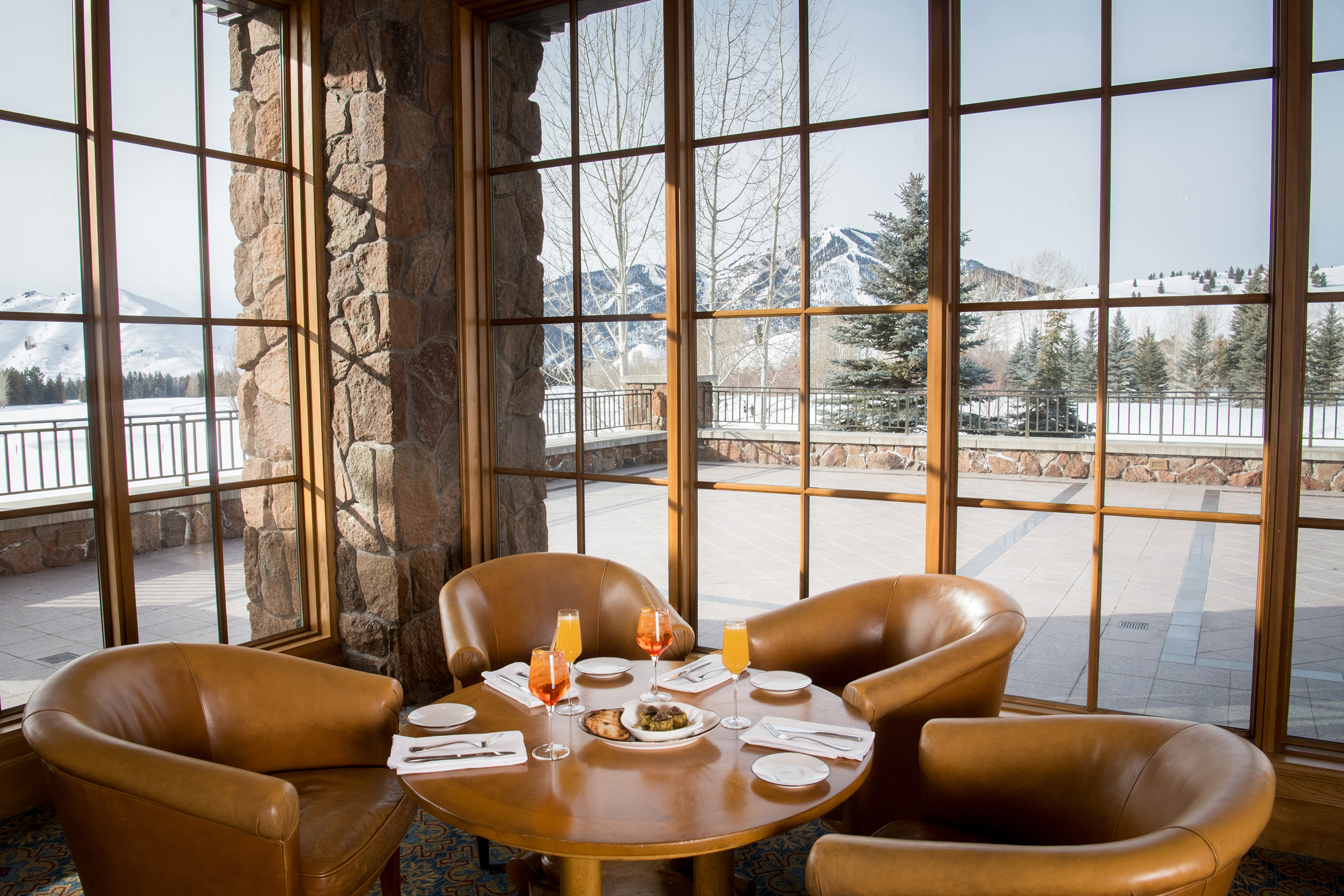 A cosy dining area in the Club House at Sun Valley with leather chairs around a wooden table set for drinks and dining, overlooking a snowy mountain landscape through large windows
