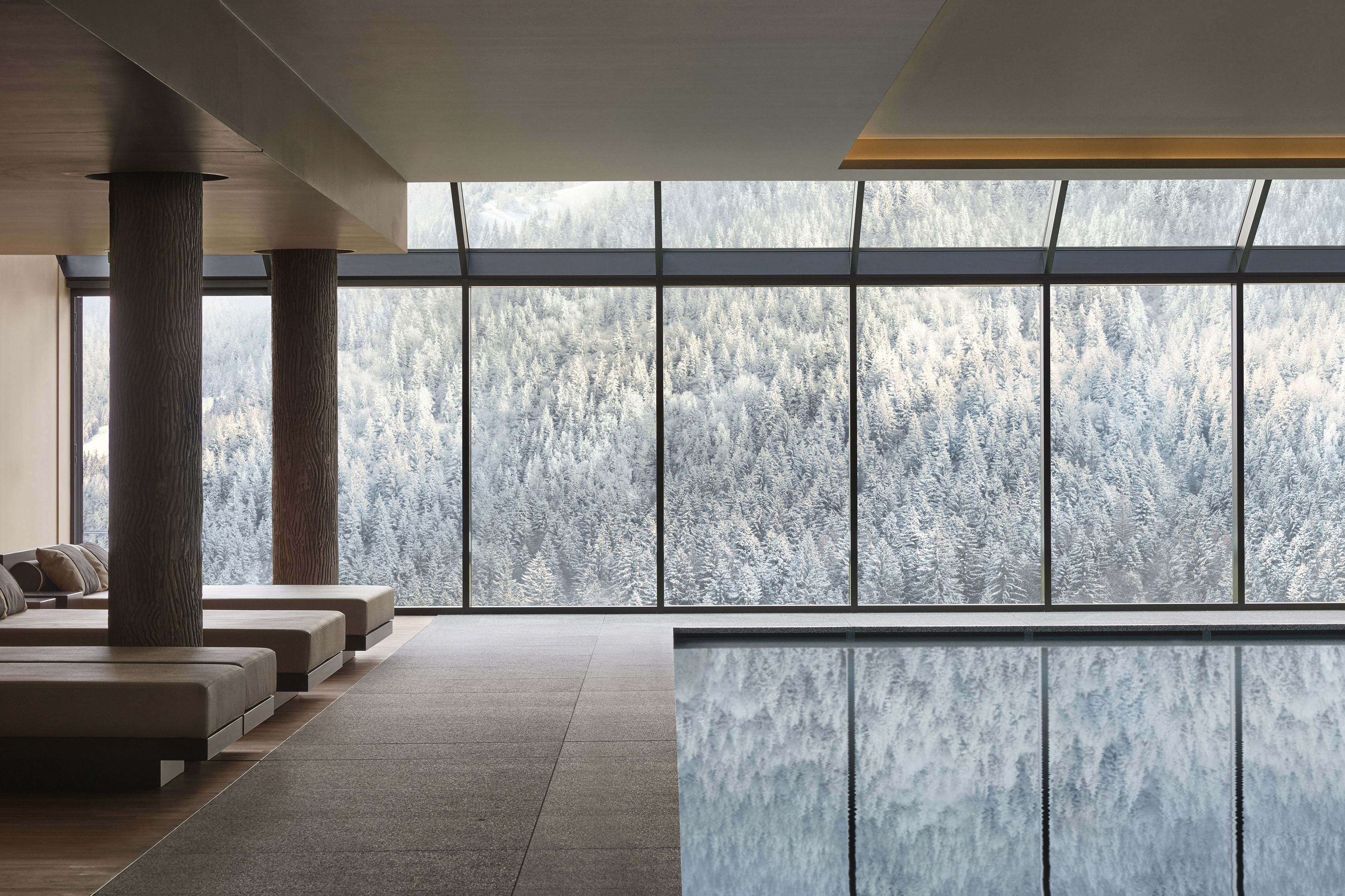 Indoor pool with view of snow-covered pine trees through floor-to-ceiling windows