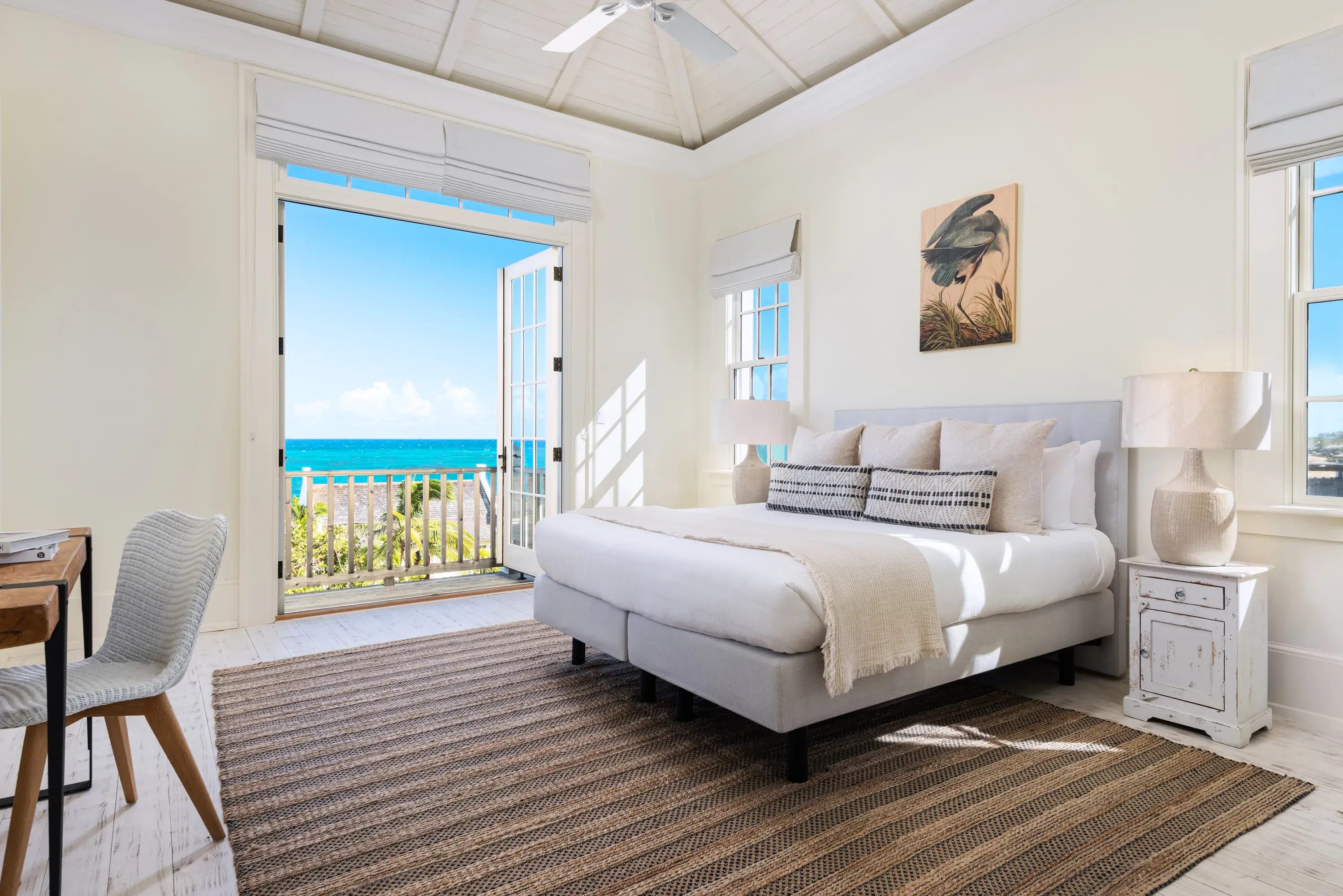 Stylish villa bedroom at Ambergris Cay in Turks & Caicos featuring pale Caribbean-style decor and large balcony windows overlooking the sea