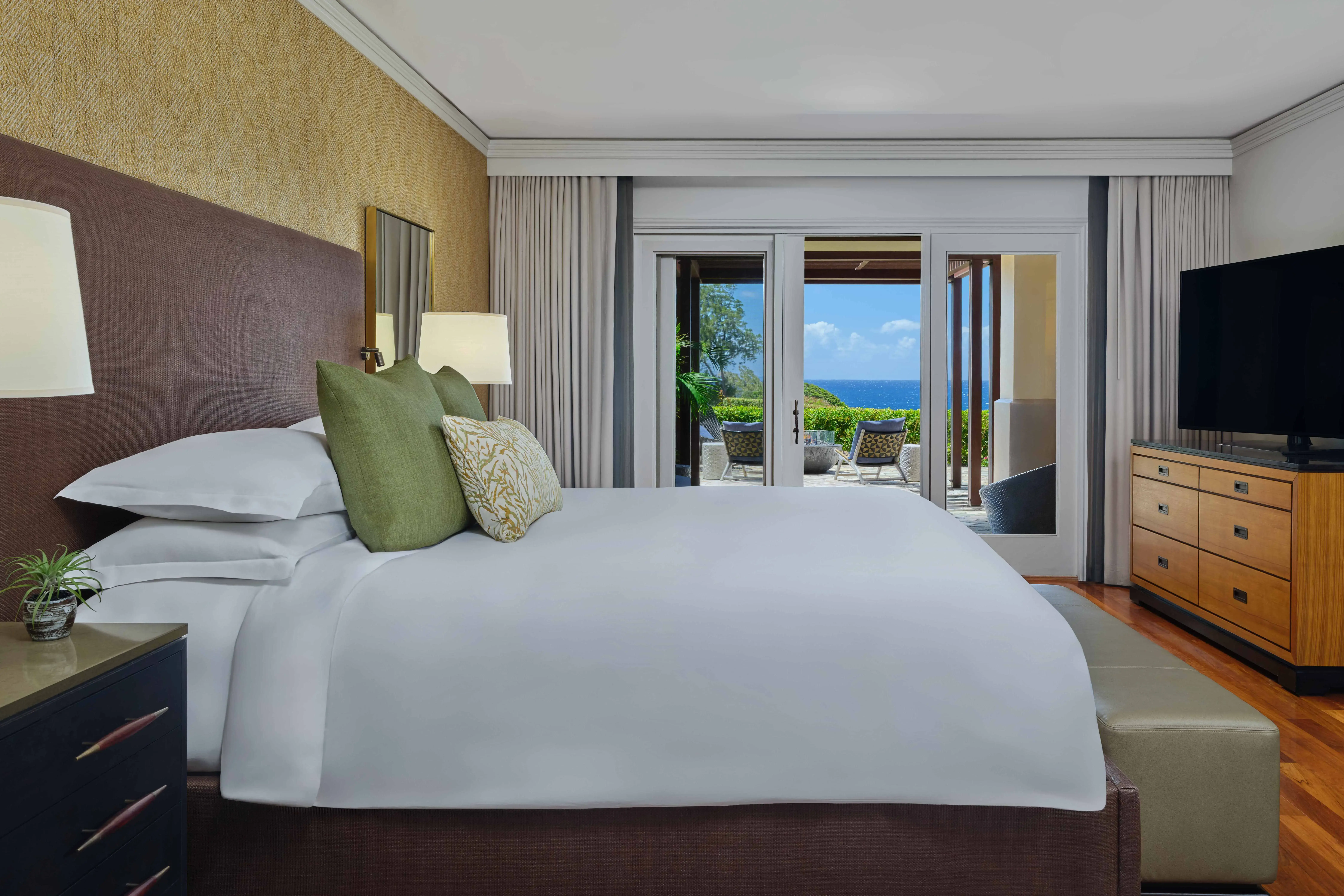 The bedroom of a Fire Lanai Suite at The Ritz-Carlton Maui, Kapula featuring a big comfy bed, drawers and tall windows looking out to sea