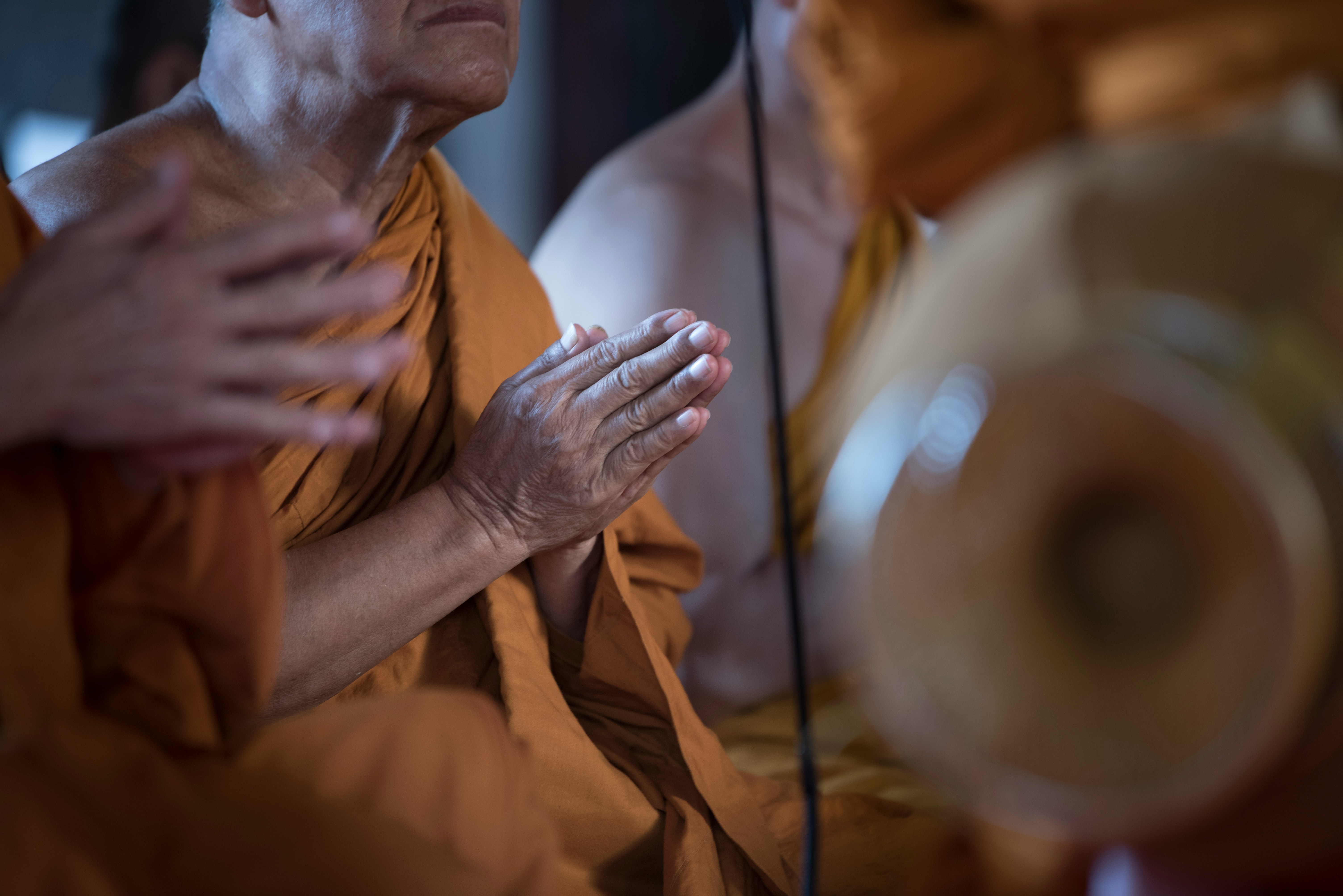 Close-up of monks in saffron robes holding their hands in a prayer gesture during a traditional ceremony.