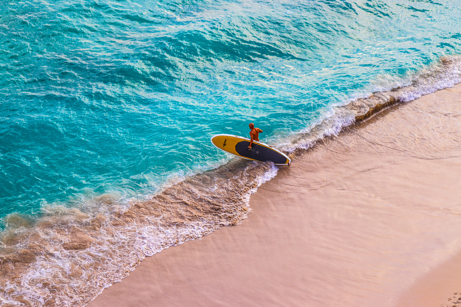 A surfer walking into the sea while holding a surfboard