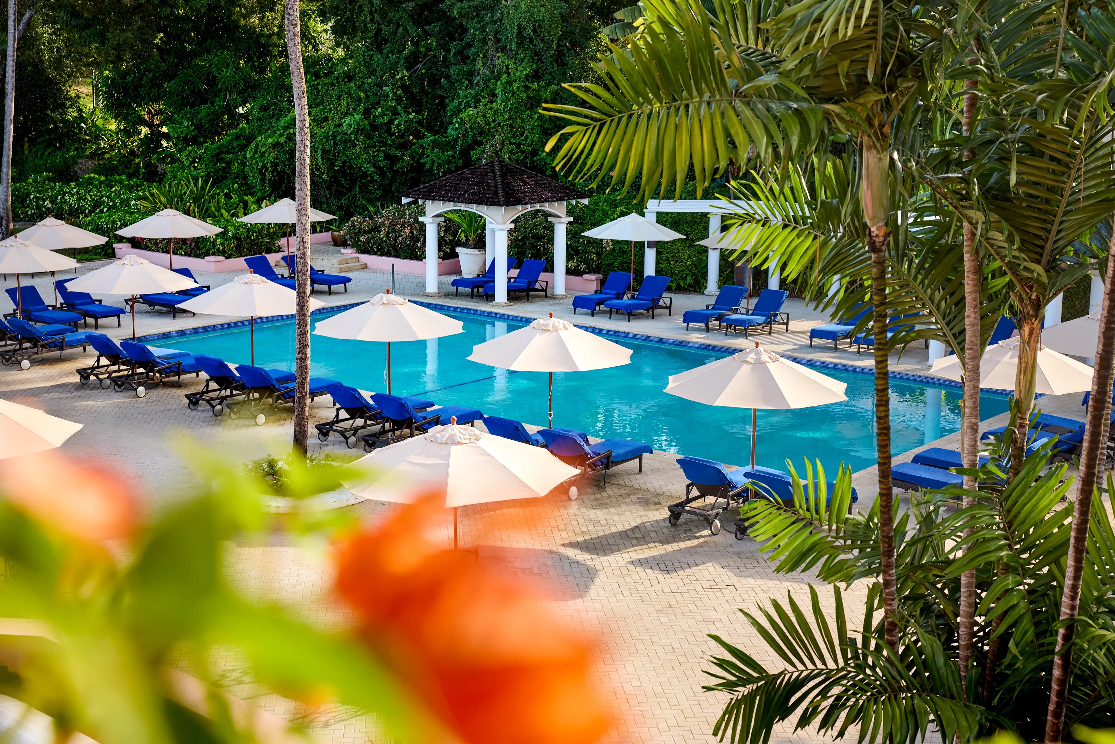 The swimming pool at Fairmont Royal Pavilion in Barbados ringed by blue sun loungers and white umbrellas surrounded by tropical gardens