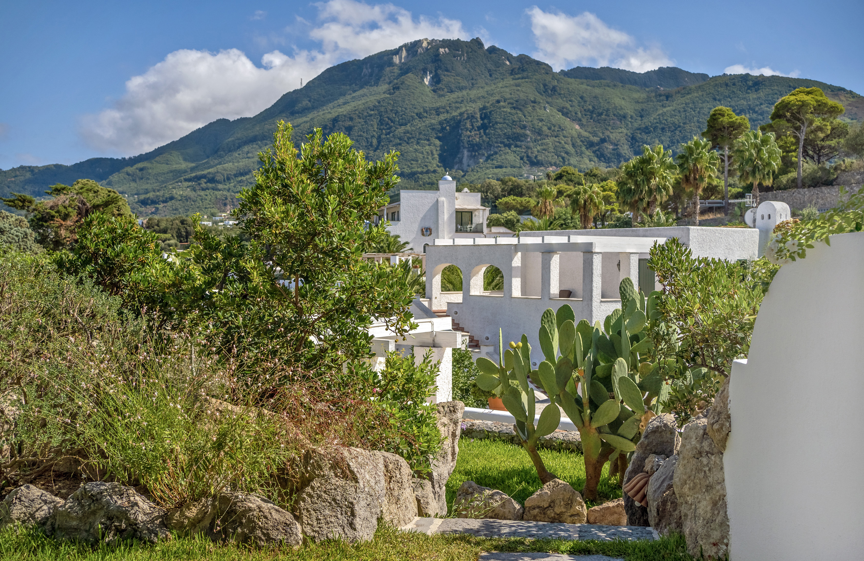 Scenic view of Botania Relais & Spa in Ischia with lush greenery, white architecture, and mountainous backdrop.