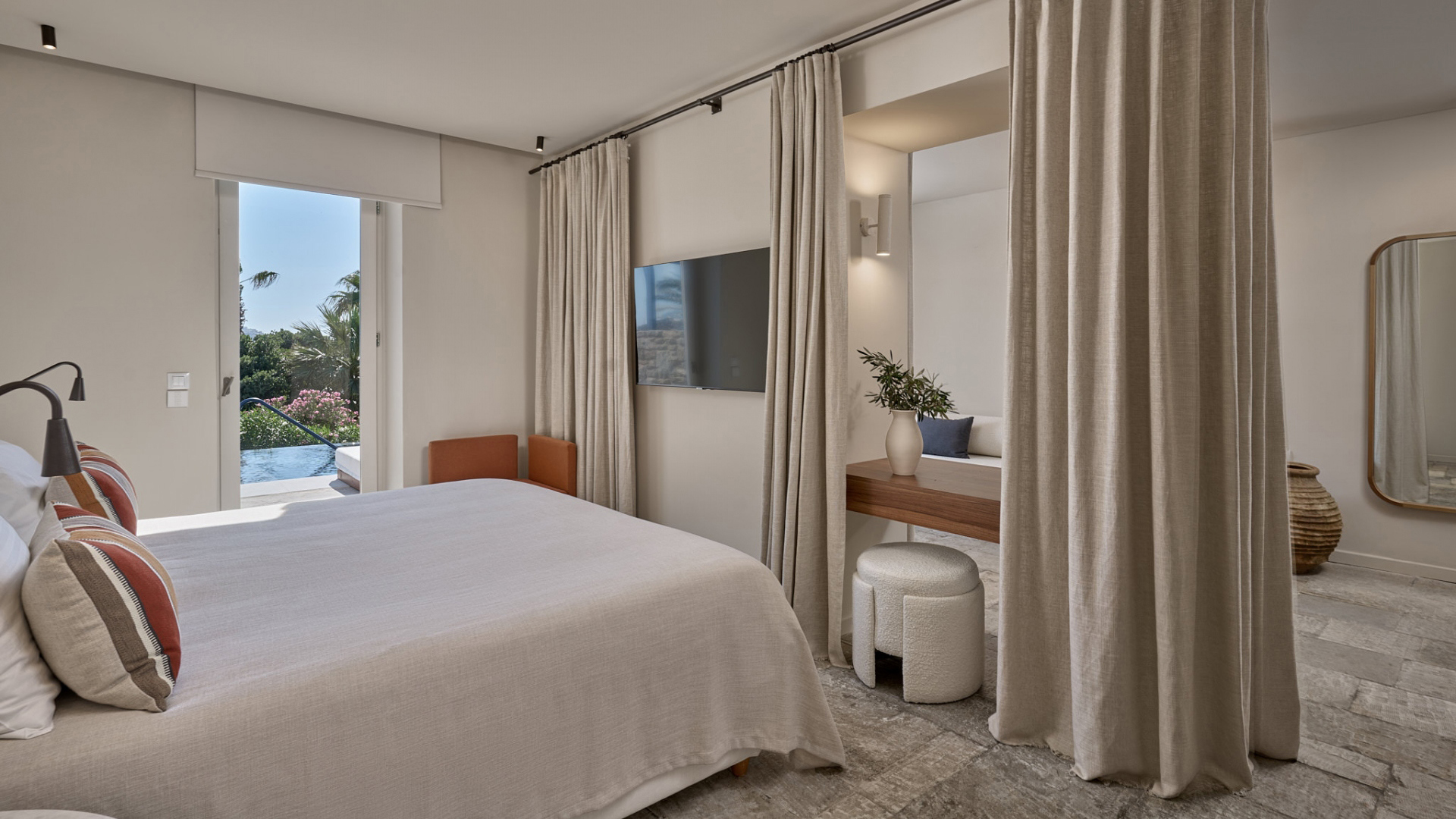 A large modern suite with neutral furniture and curtains with a view of the pool and greenery through the door