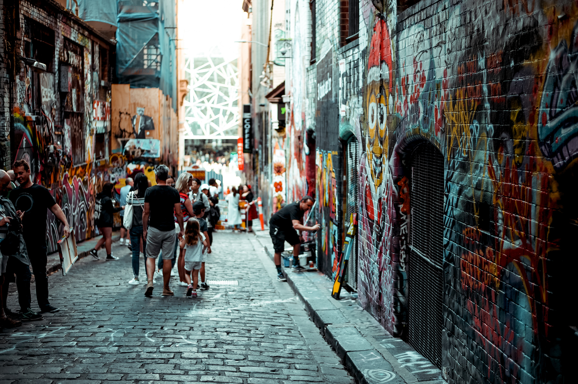 A busy brick road street with the building walls covered in street art, Melbourne