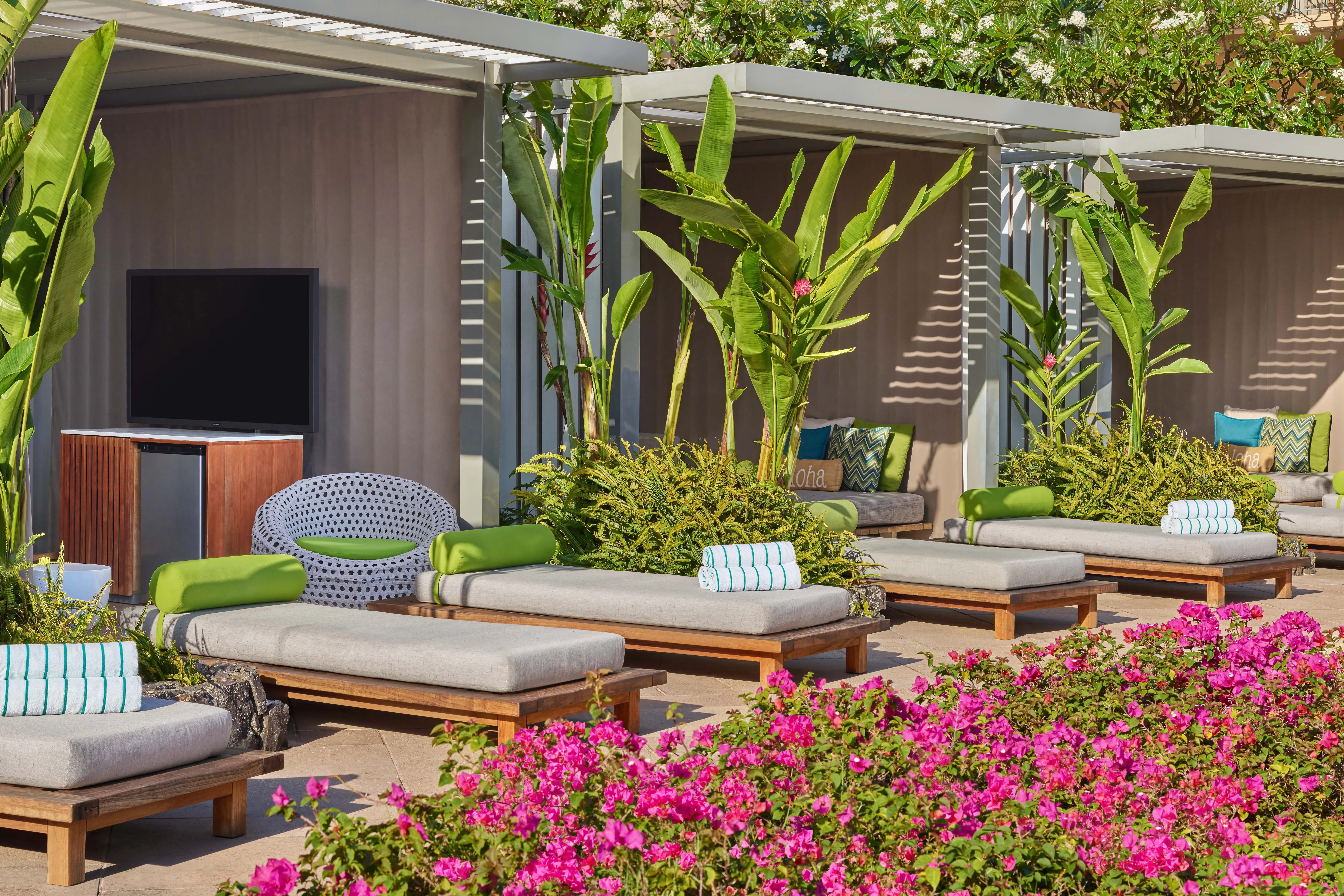 Stylish pool cabanas at The Ritz-Carlton Maui, Kapalua featuring tall plants and comfy sun loungers behind pink flowers