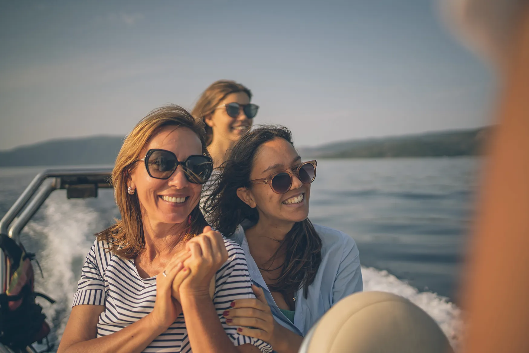 People wearing sunglasses enjoying a speedboat ride on calm coastal waters.