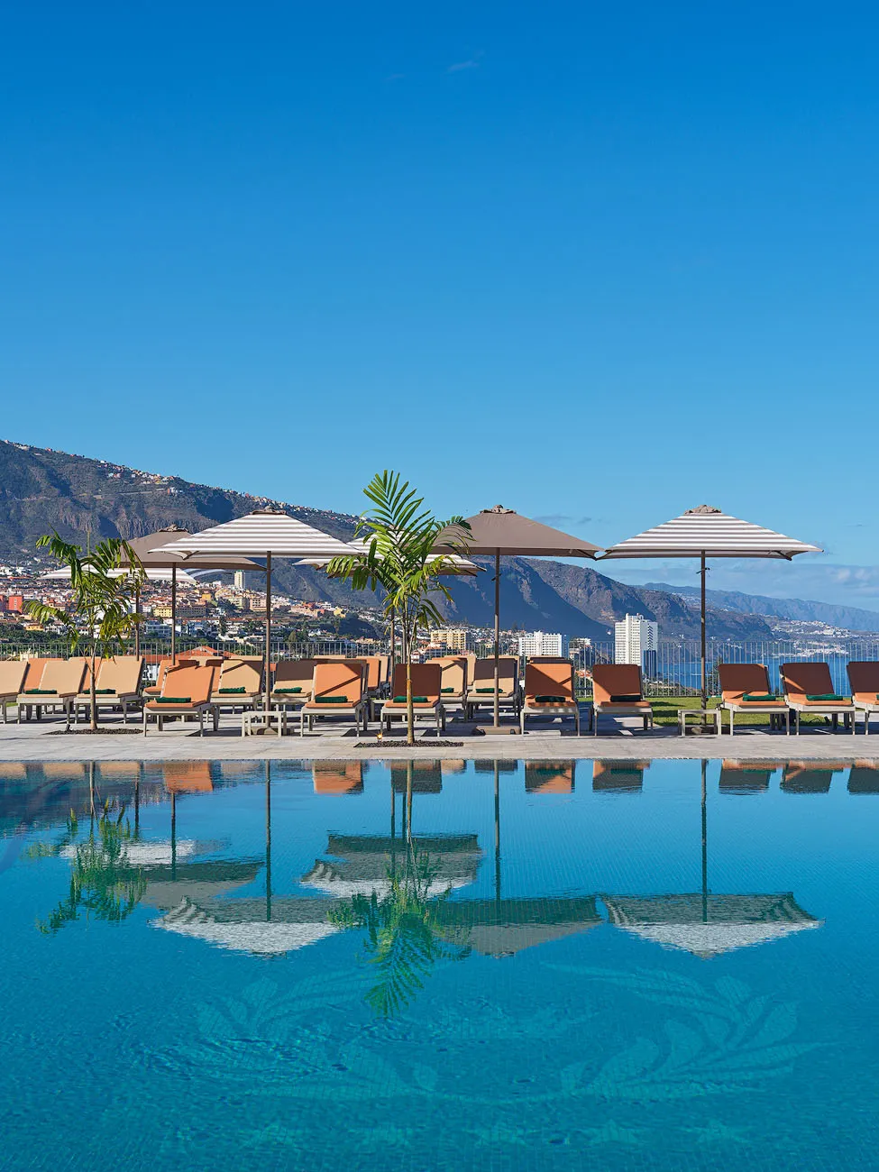 Infinity pool at Gran Hotel Taoro in Tenerife with sun loungers, parasols and panoramic views of the coastline and mountains.