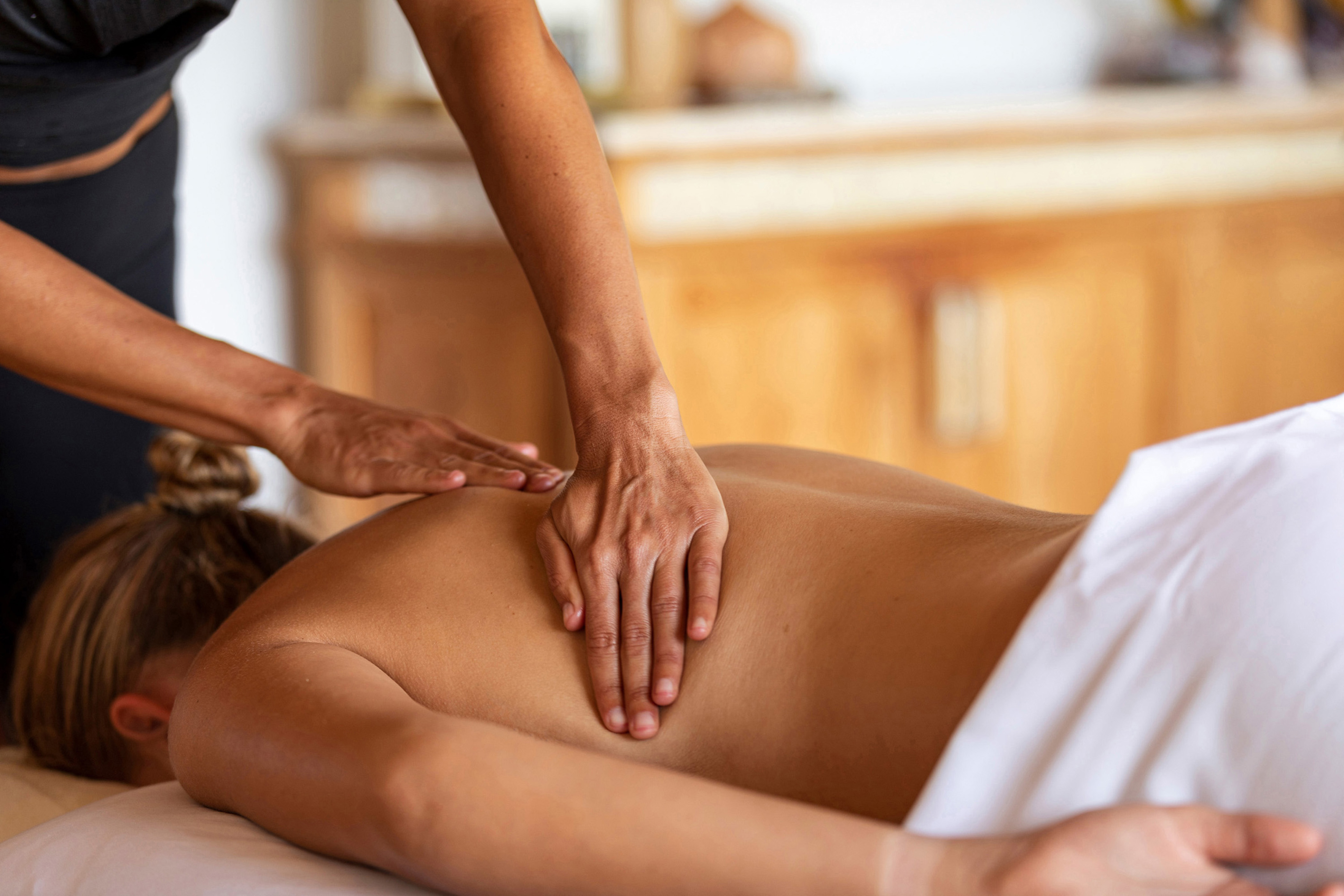 A blond woman lying on a massage table while a therapist massages her back