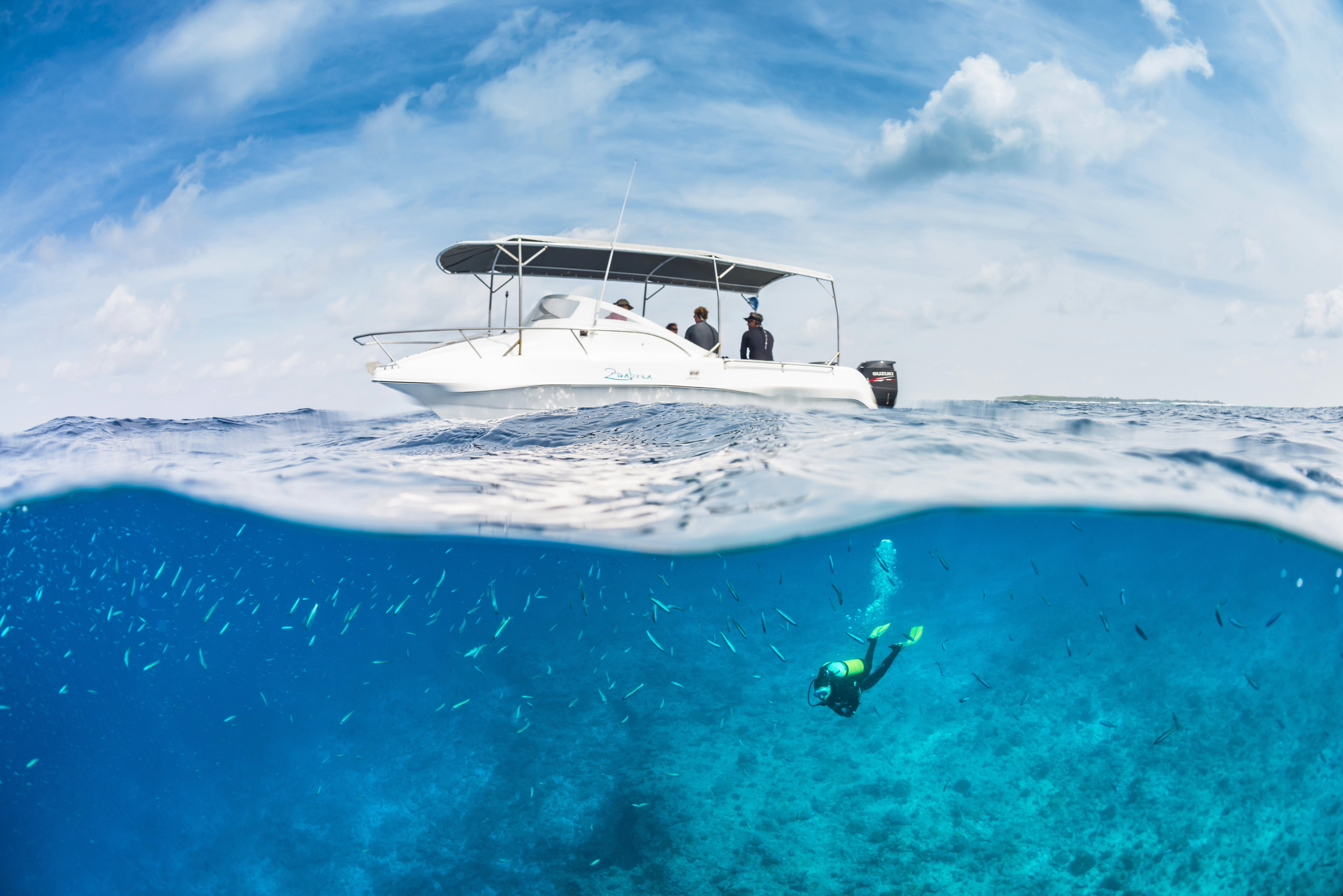 A boat bobbing on the surface of the ocean with a diver swimming down to a school of fish