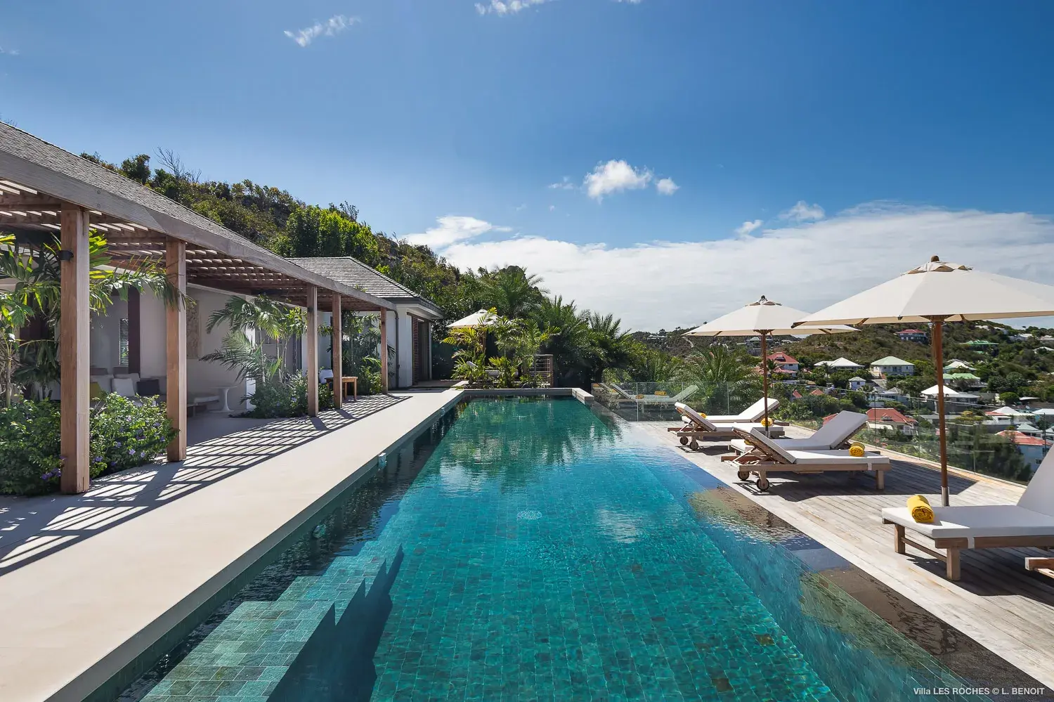 Luxury infinity pool at Les Roches Villa in St Barths with sun loungers, tropical gardens and panoramic hillside views.