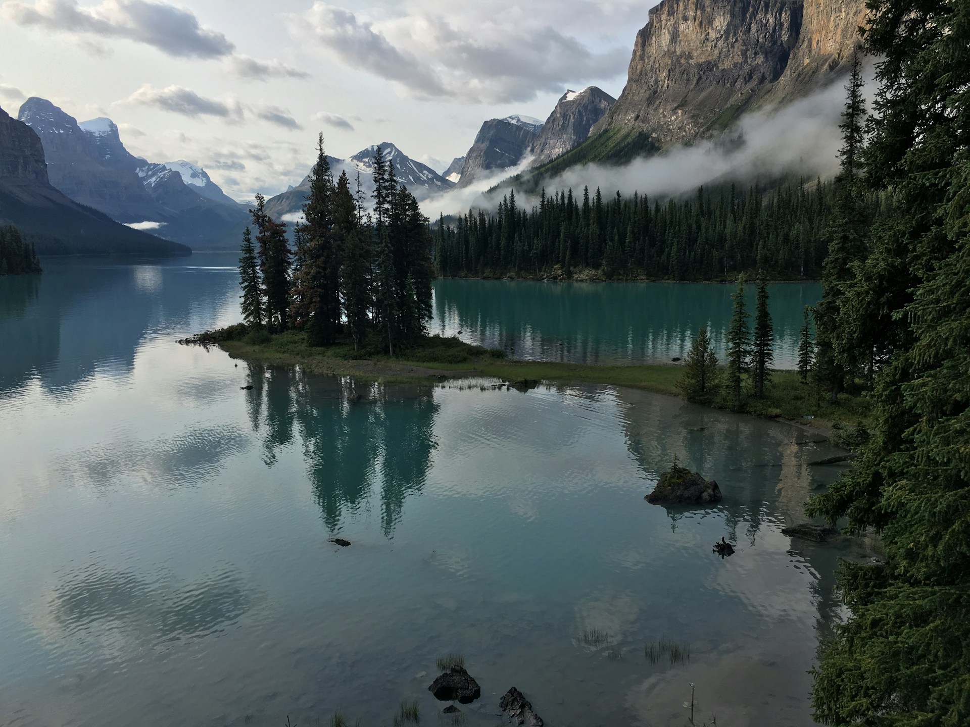The serene Lake Maligne in Canada surrounded by mountains and dense forest, with a small island of trees in the middle