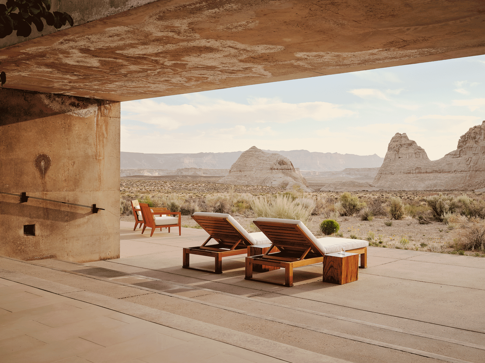 Minimalist desert terrace with wooden loungers overlooking sculptural rock formations and open skies.