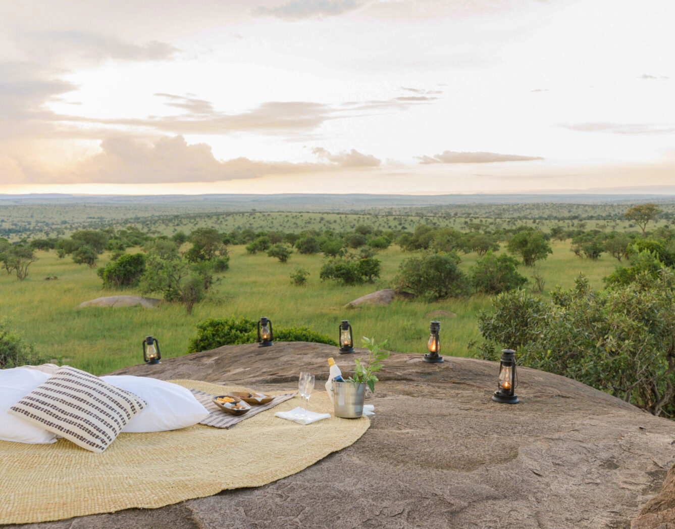 A luxury picnic with candles set up on top of a rock formation with sweeping views of the Serengeti