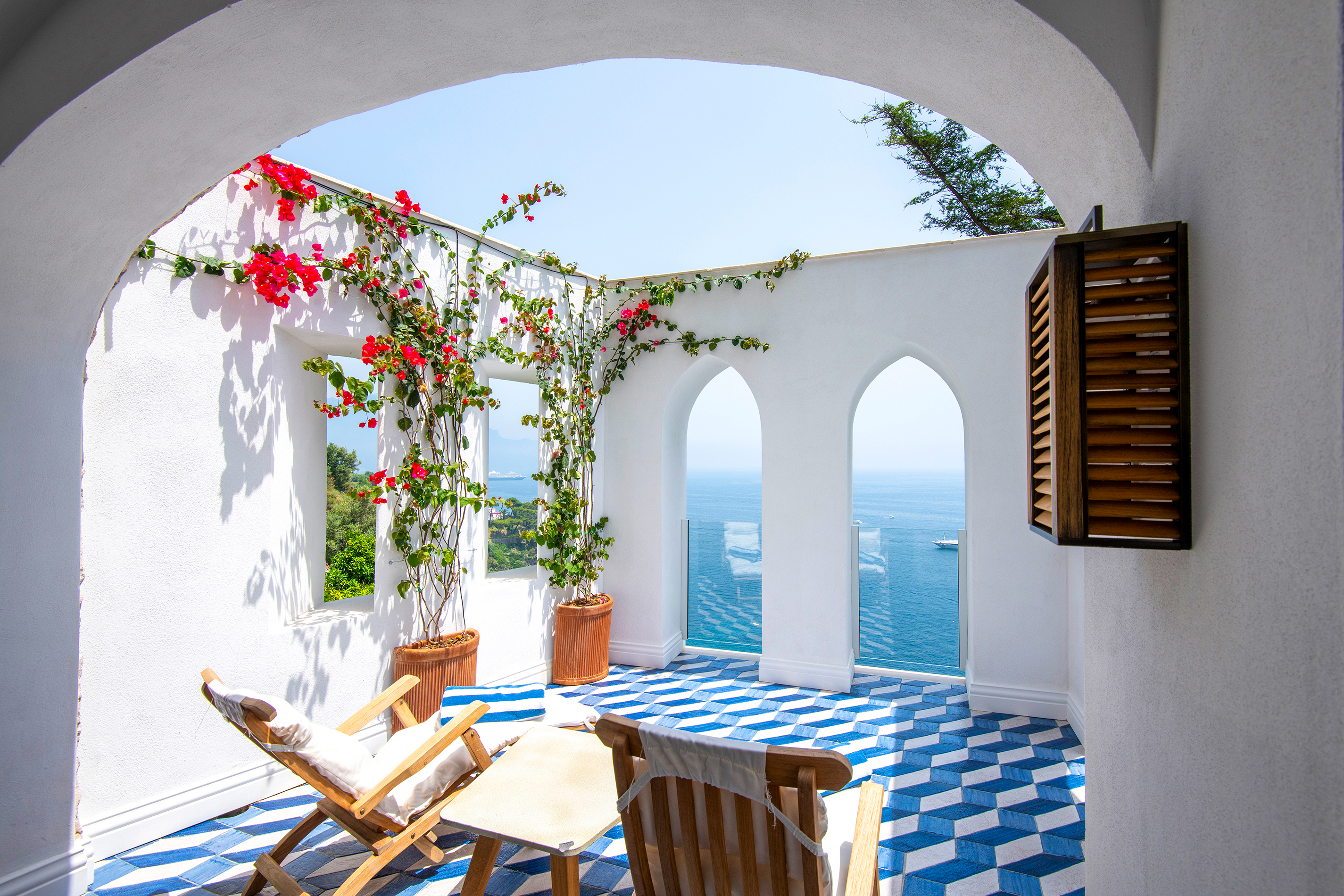 Scenic corner suite terrace at Borgo Santandrea in Amalfi featuring vibrant bougainvillea, elegant seating, and panoramic ocean views.
