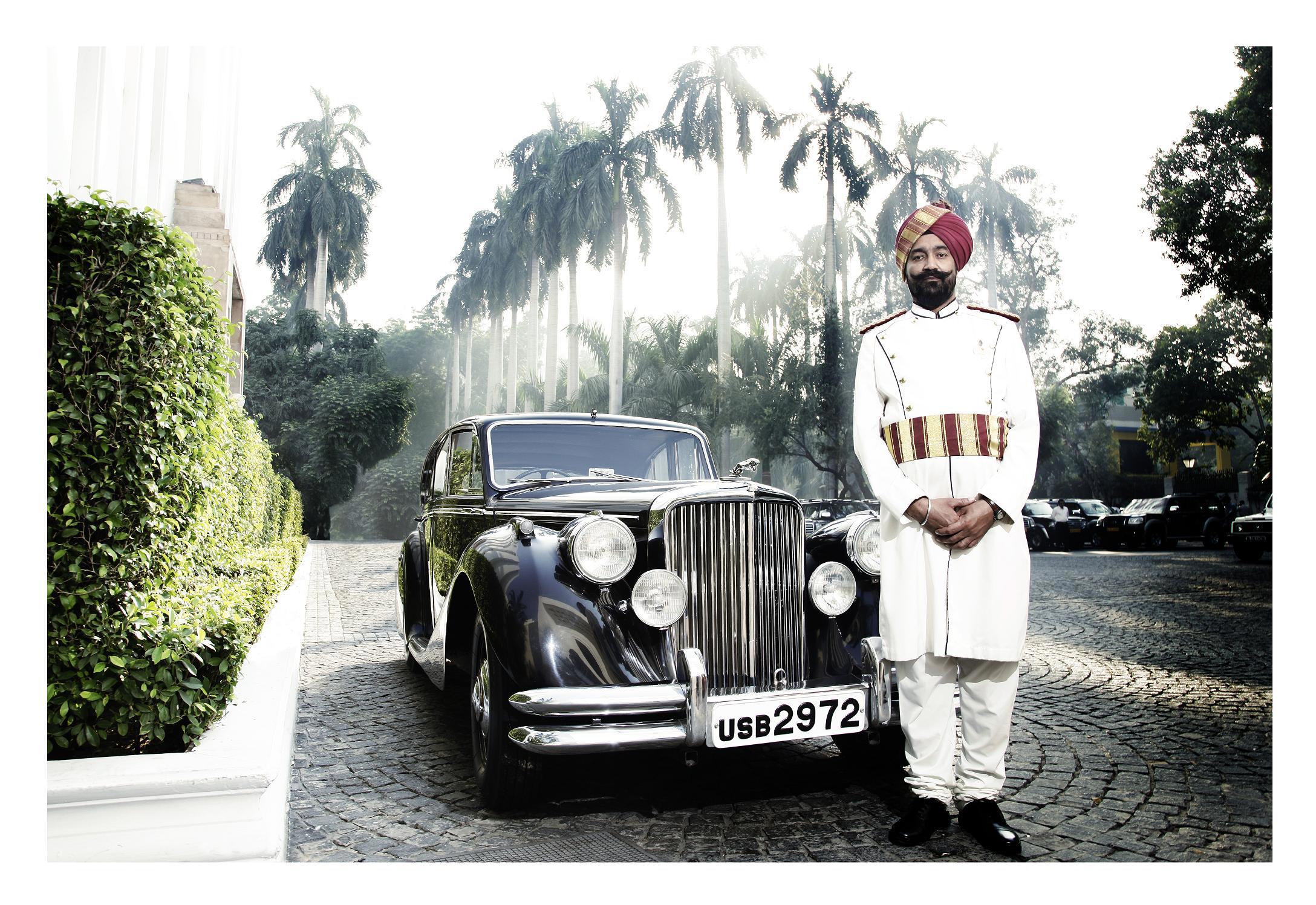 Man in traditional dress standing in front of a black classic car on a cobbled driveway