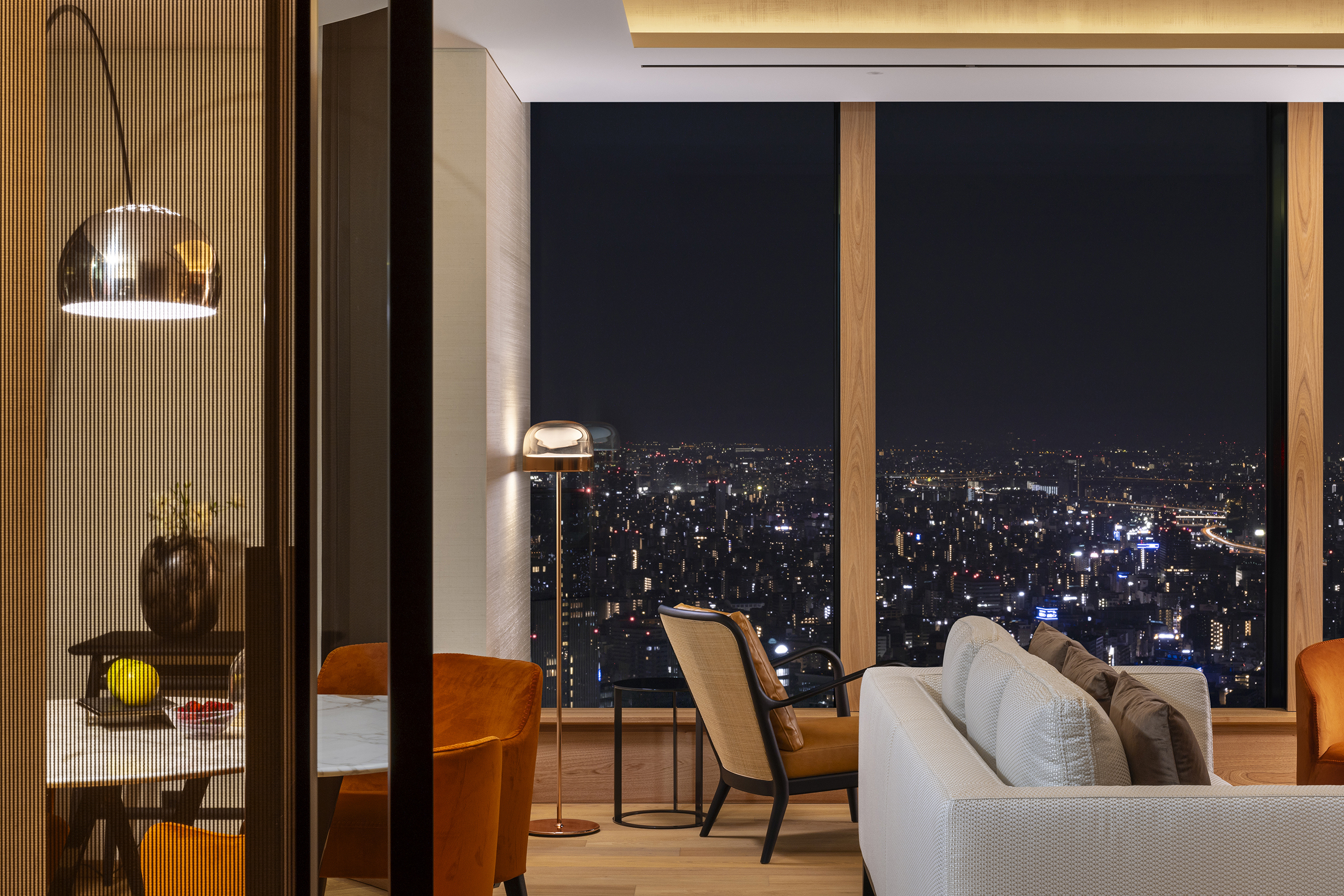 Modern furniture details of a suite at Bulgari Tokyo featuring white and orange sofas, sleek circular lamps and views of the city at night