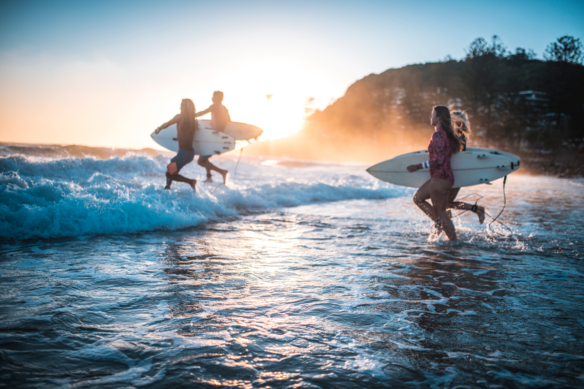 A group of people running into the sea with surfboards