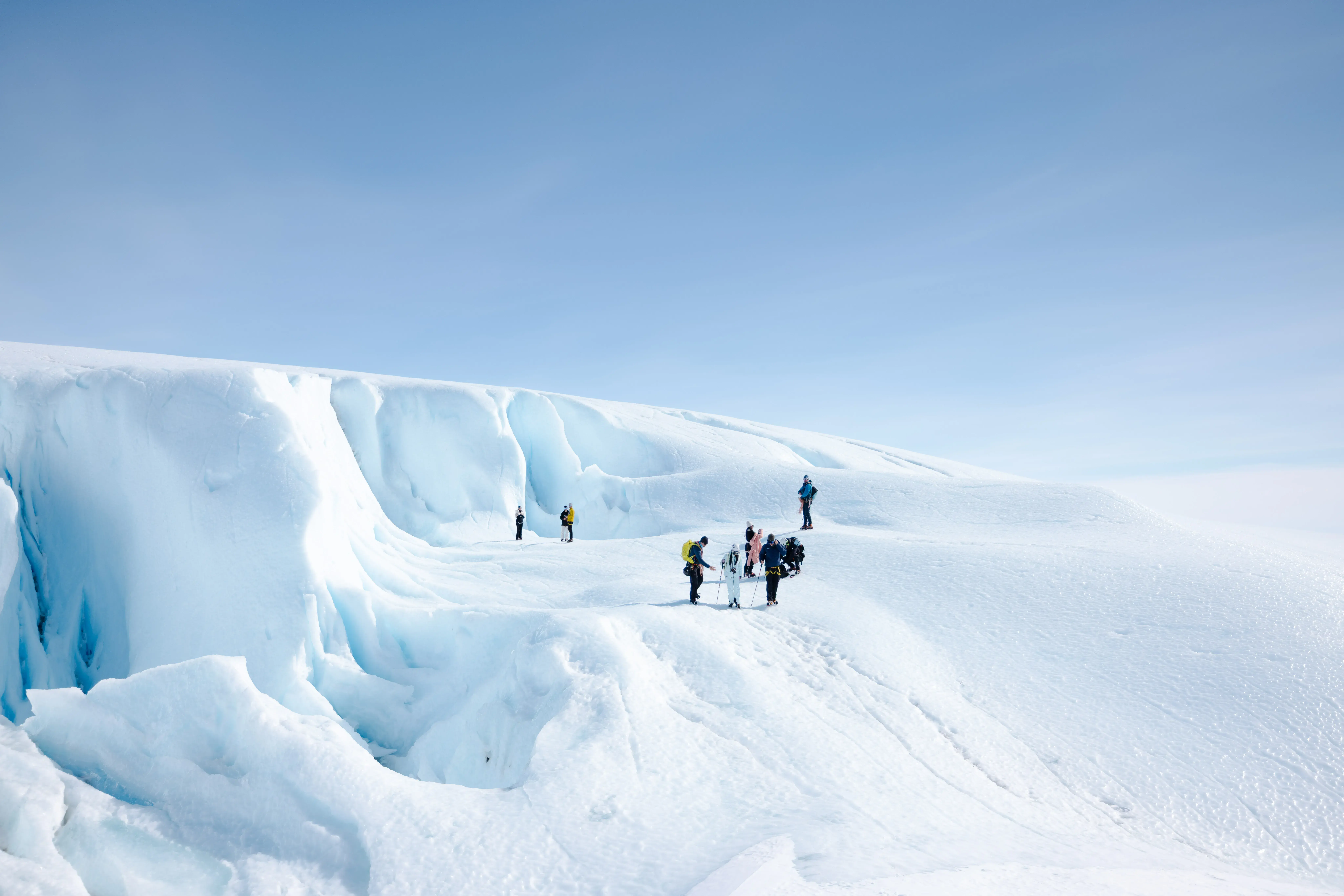 A group of hikers atop an icy glacier under a clear sky.